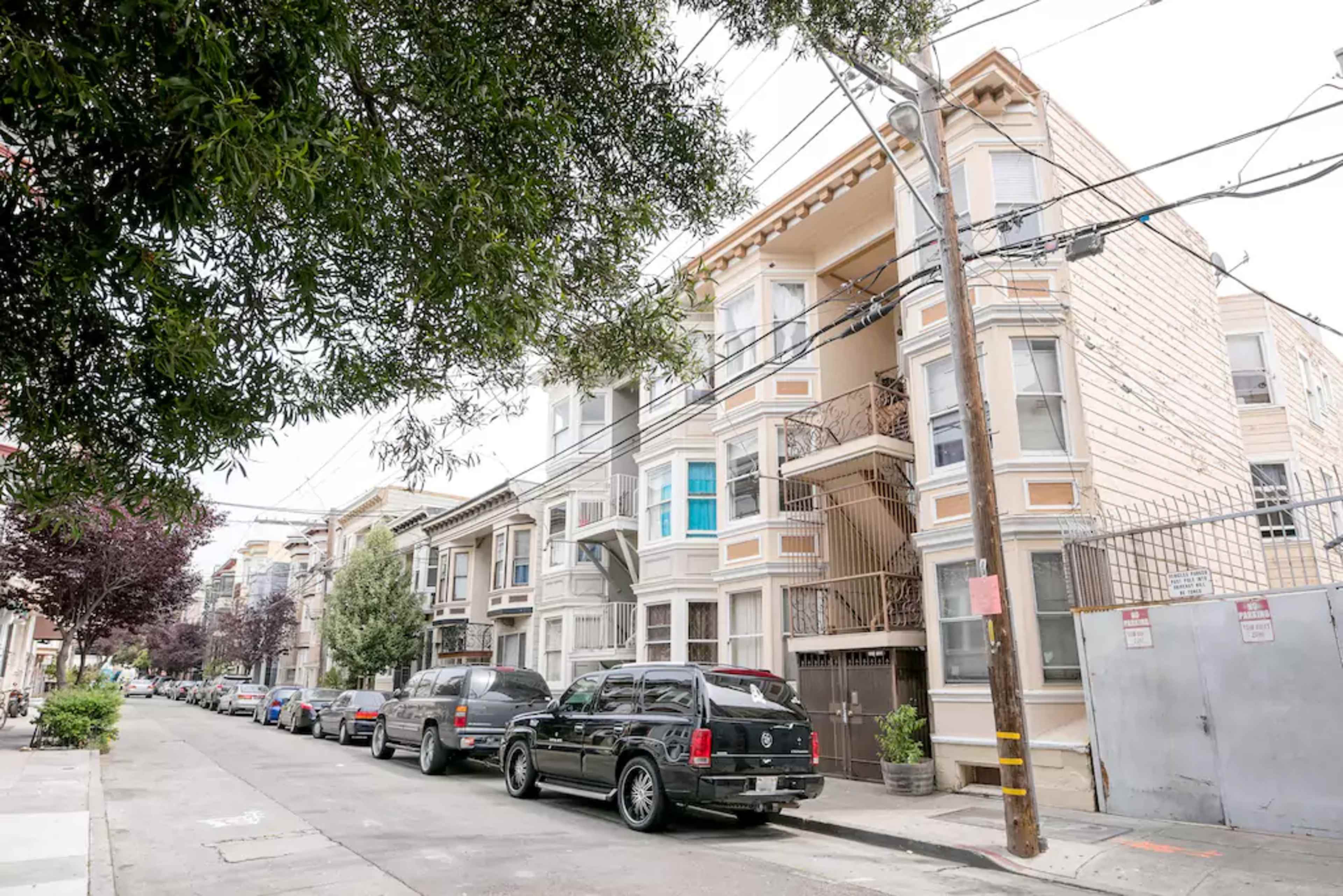 A street view features a row of multi-story apartment buildings facing a lined street with parked cars.