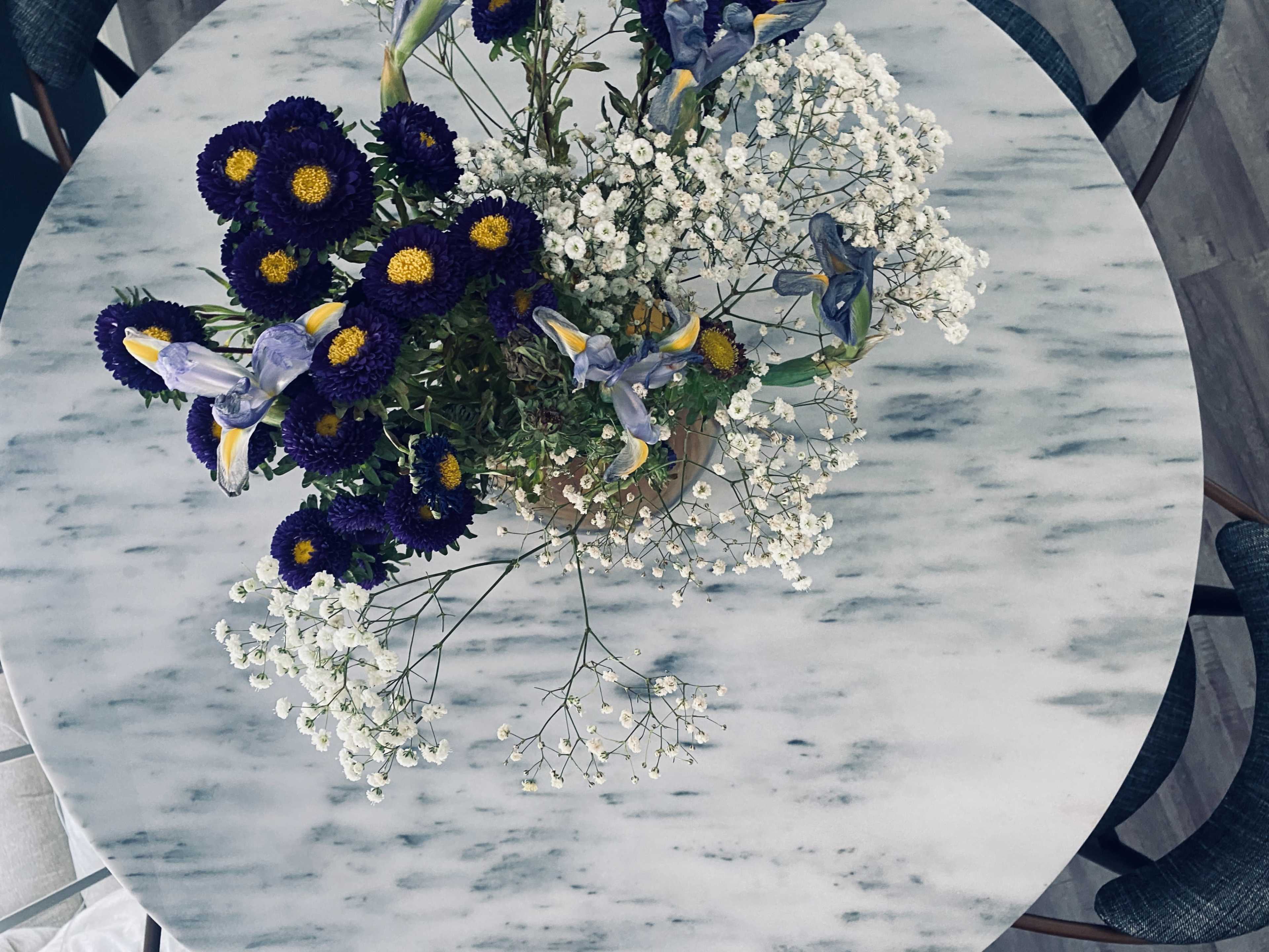 A round marble table is topped with a vase of purple and white flowers.