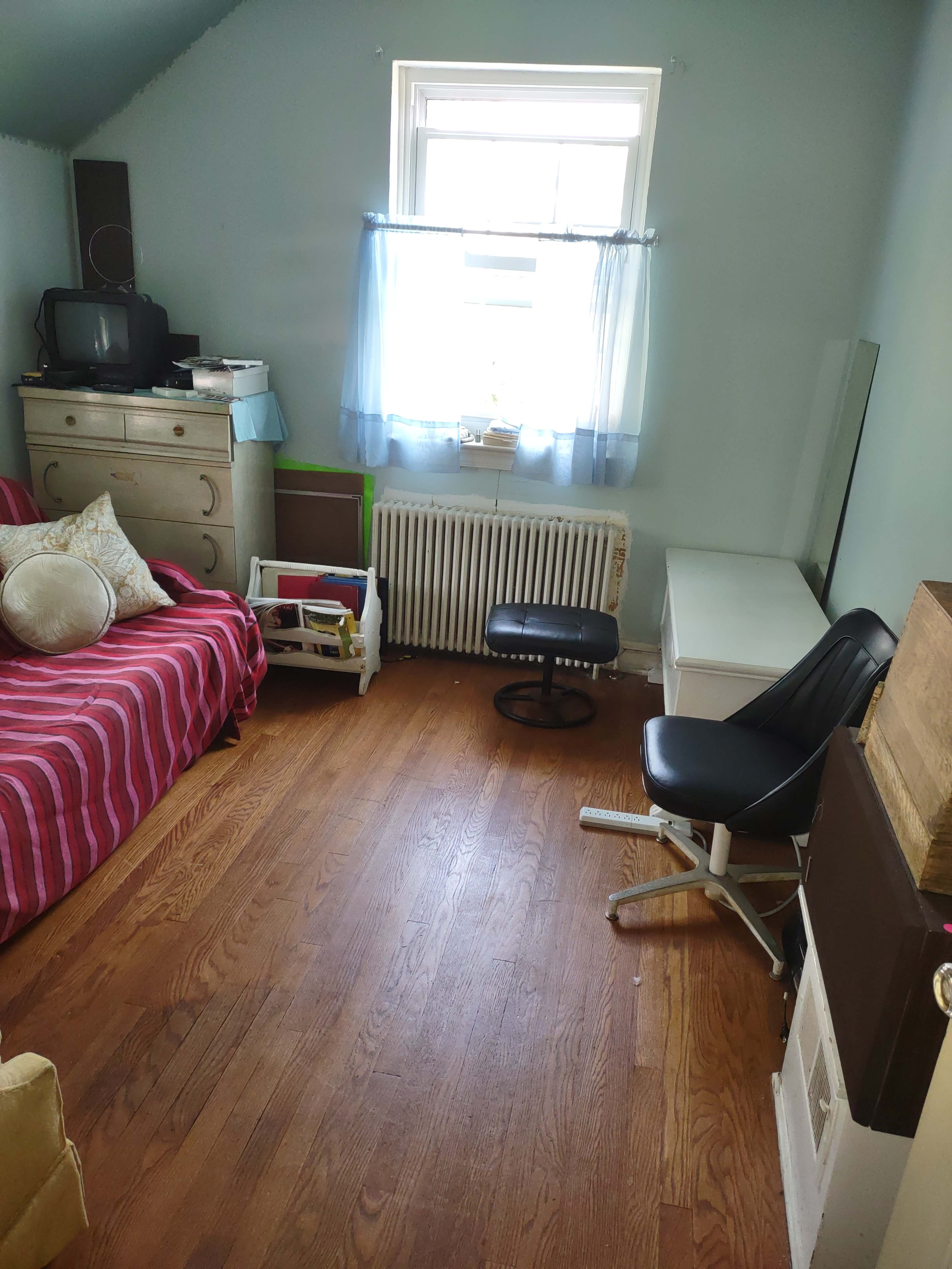 A room with a red-striped sofa, a television on a dresser, a white table, a chair, and a window with blue curtains.