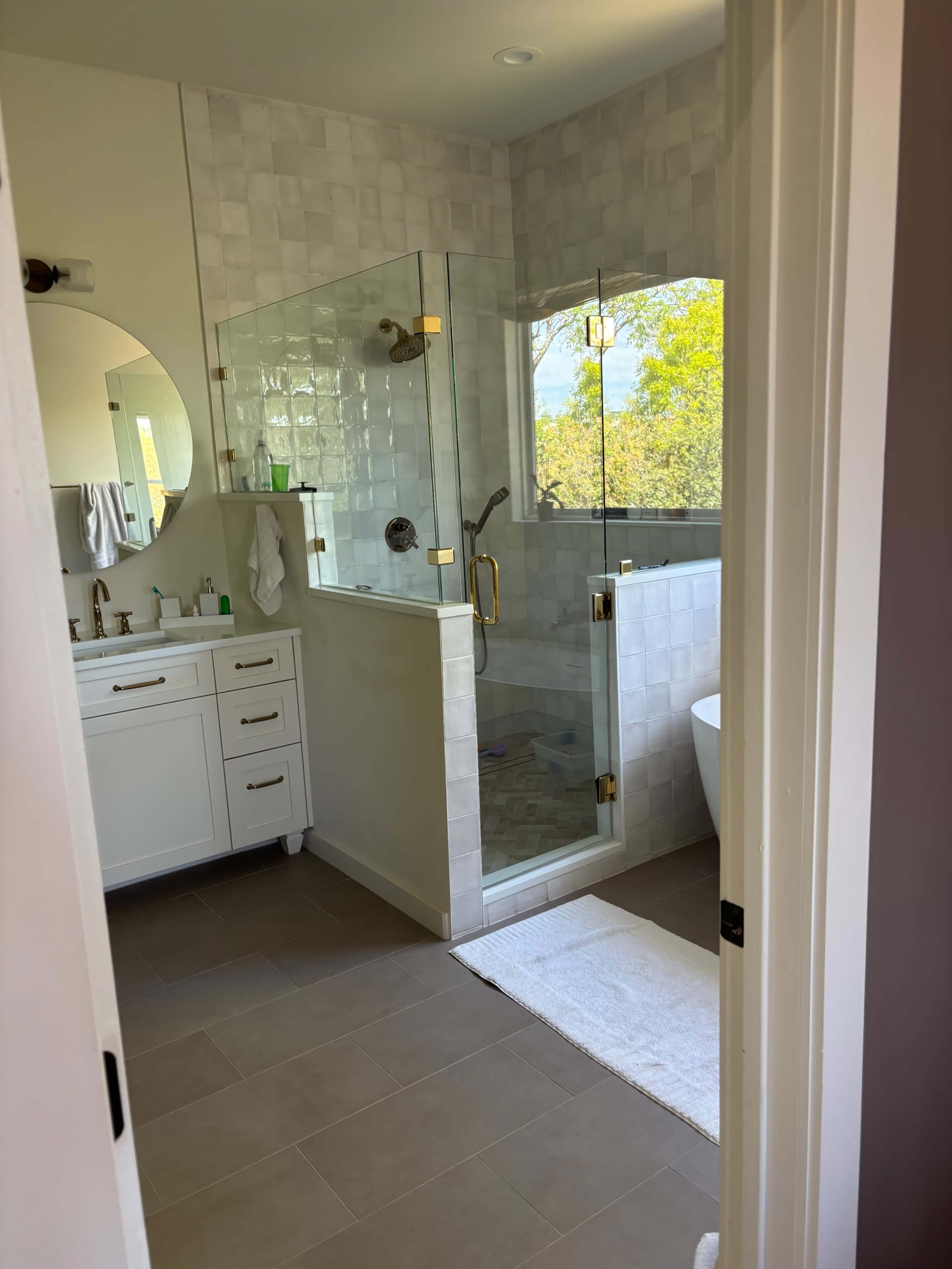 The image shows a modern bathroom featuring a glass shower enclosure, a freestanding bathtub, and a vanity with multiple sinks.