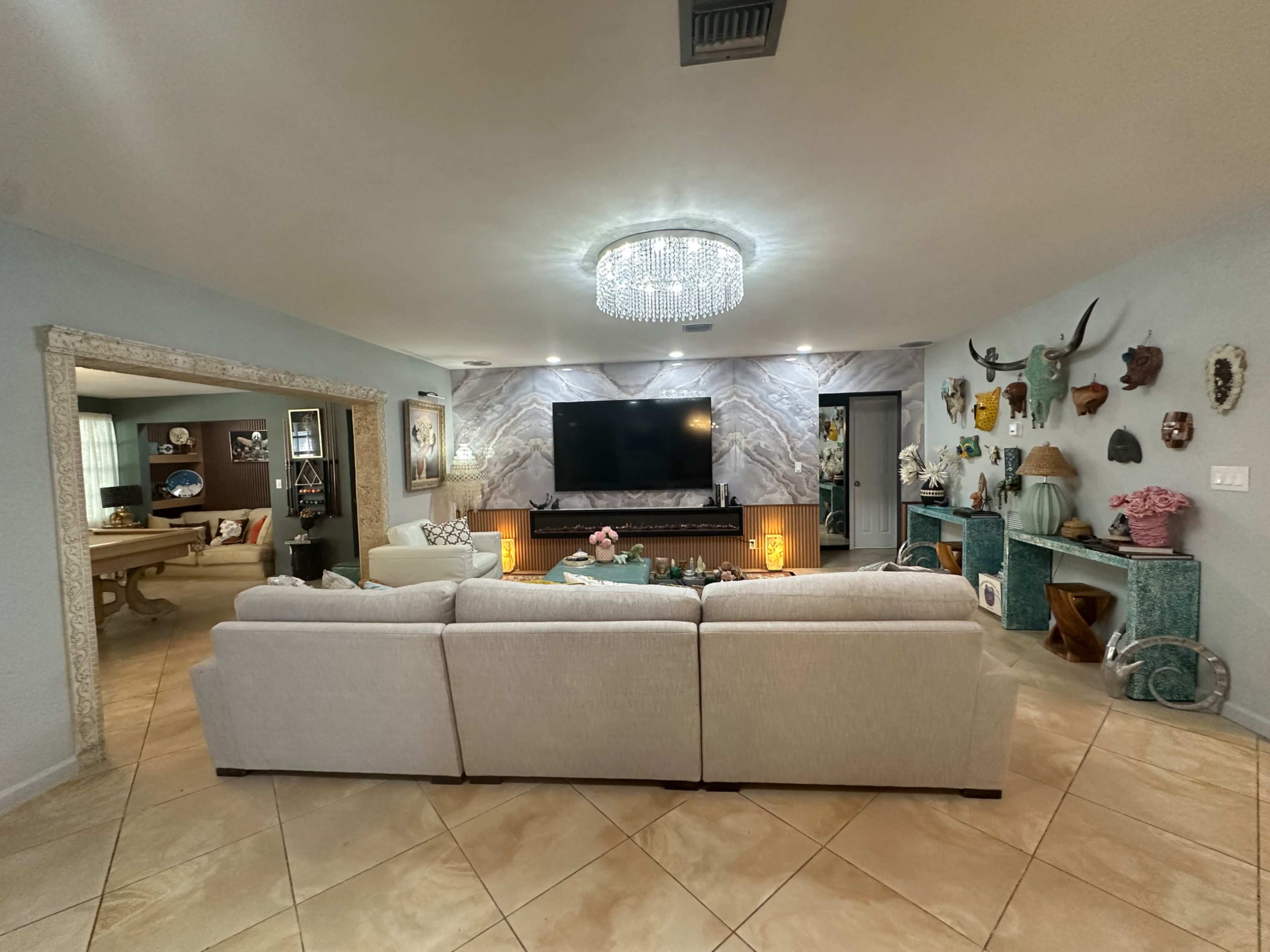 The living room features a light-colored sectional sofa, a mounted flat-screen TV, and decorative wall elements including animal heads and artworks.