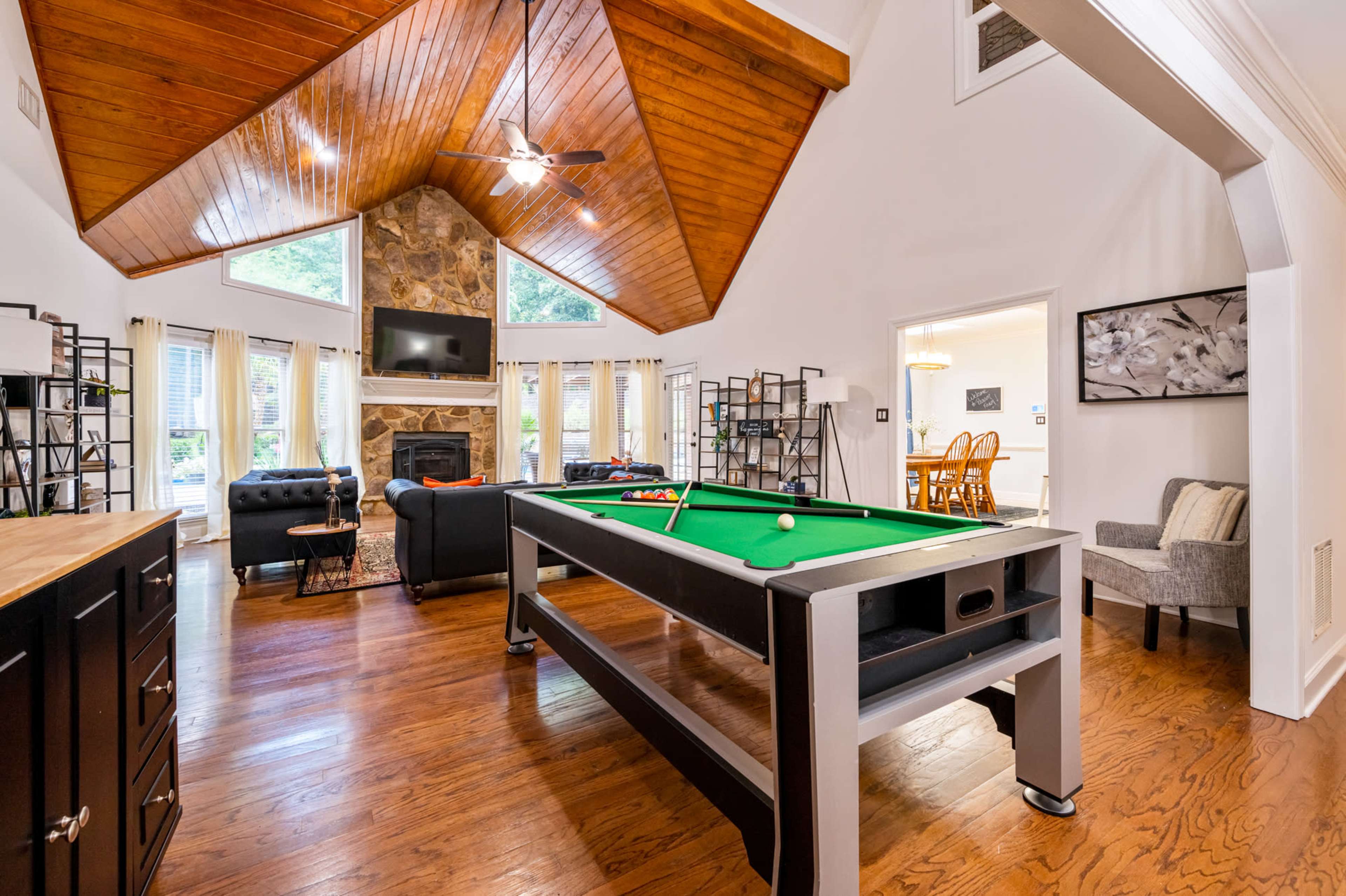 A spacious living area features a pool table, a stone fireplace, and large windows that allow natural light to fill the room.