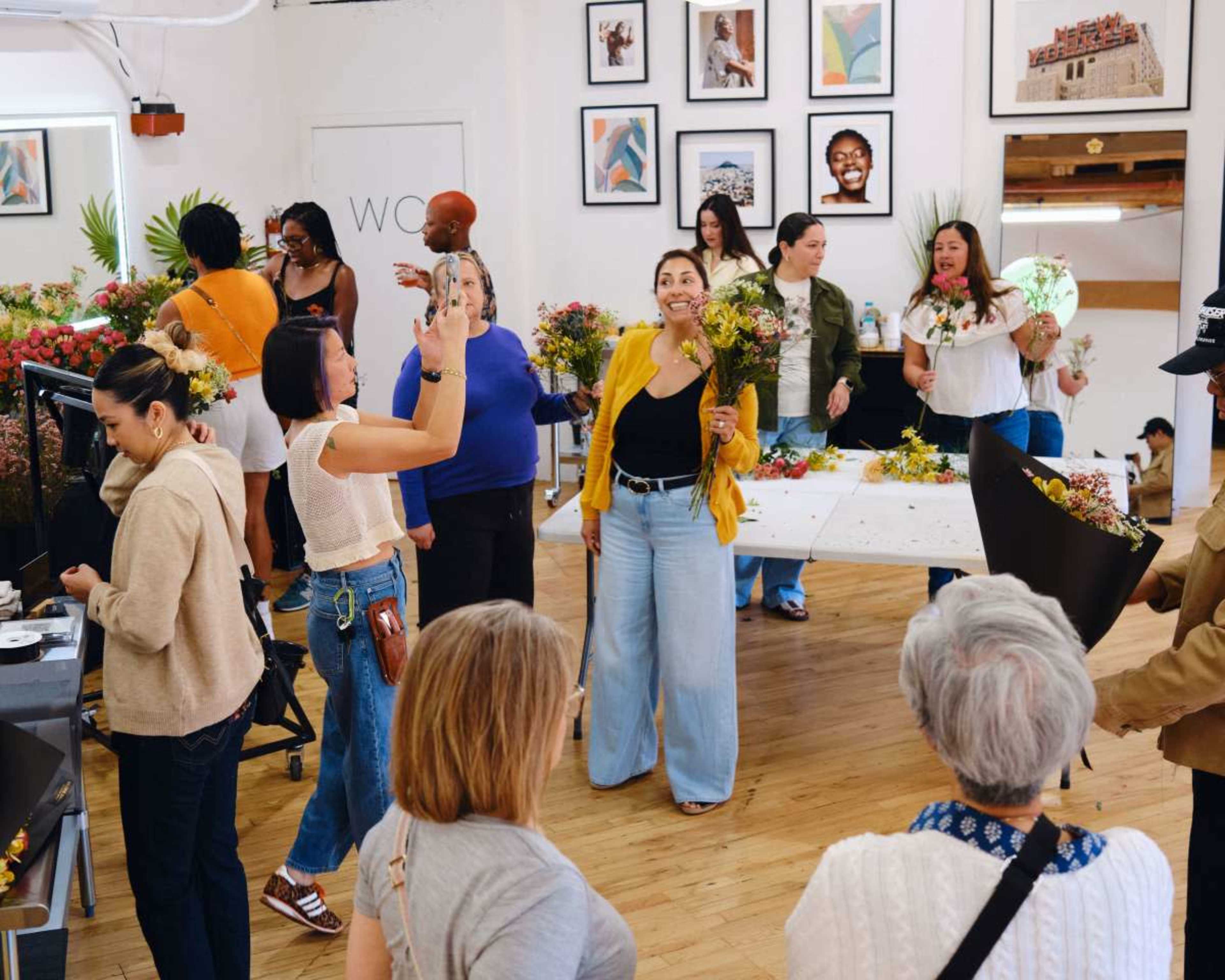 A group of people is gathered in a bright room, engaging in a floral arranging workshop while holding bouquets of flowers.