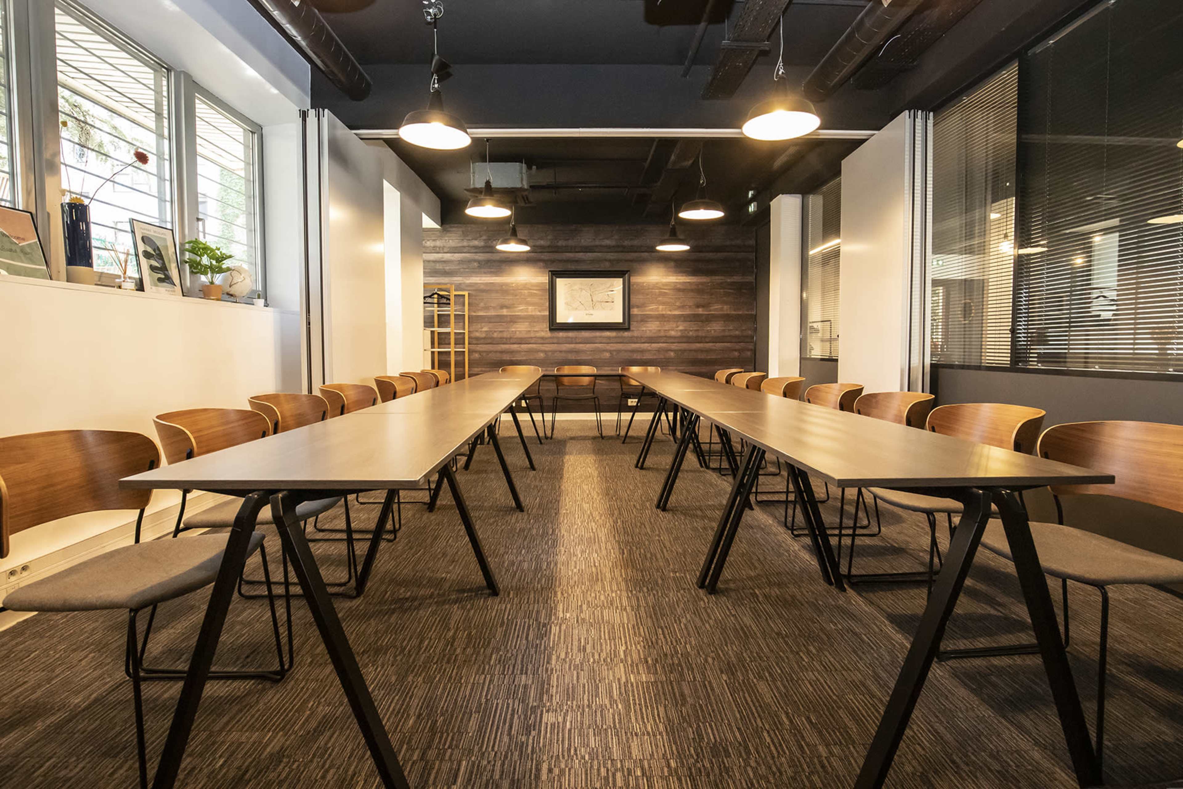 A conference room features two rows of wooden tables with chairs, illuminated by ceiling lights.