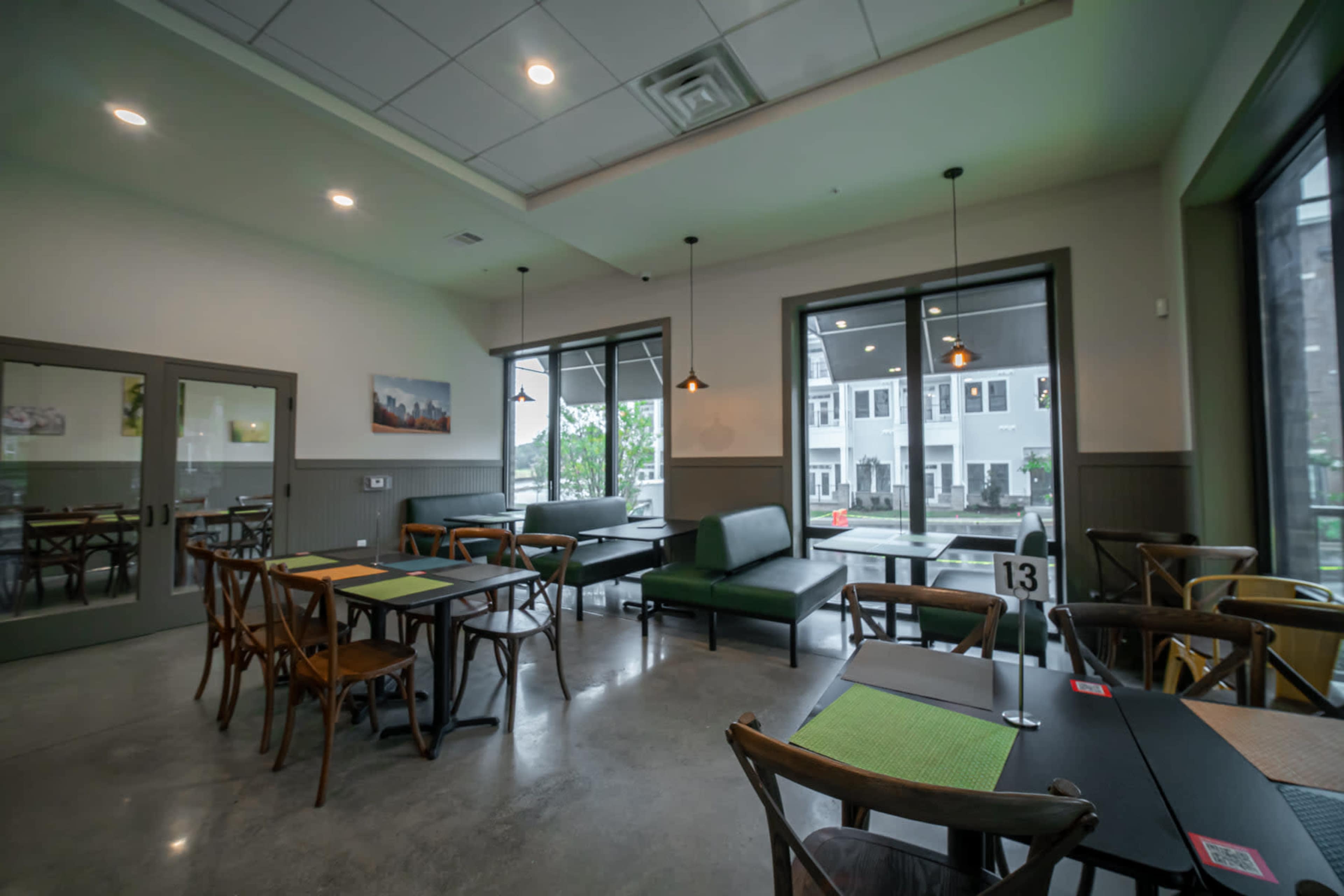 The image shows a modern restaurant interior featuring several tables, a green sofa, and large windows allowing natural light.
