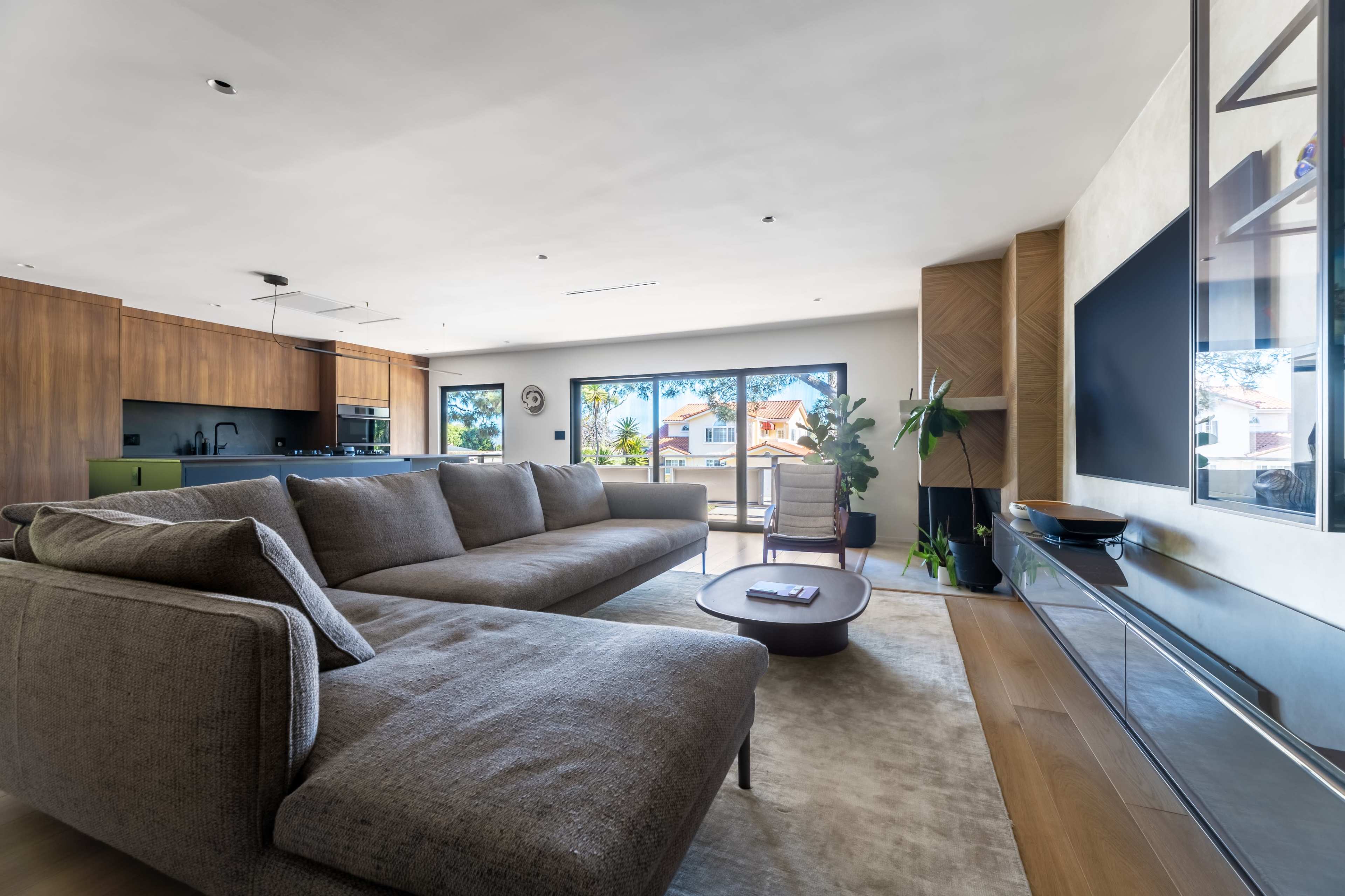 A modern living room features a large sectional sofa, a round coffee table, and expansive windows providing views of an outdoor area.