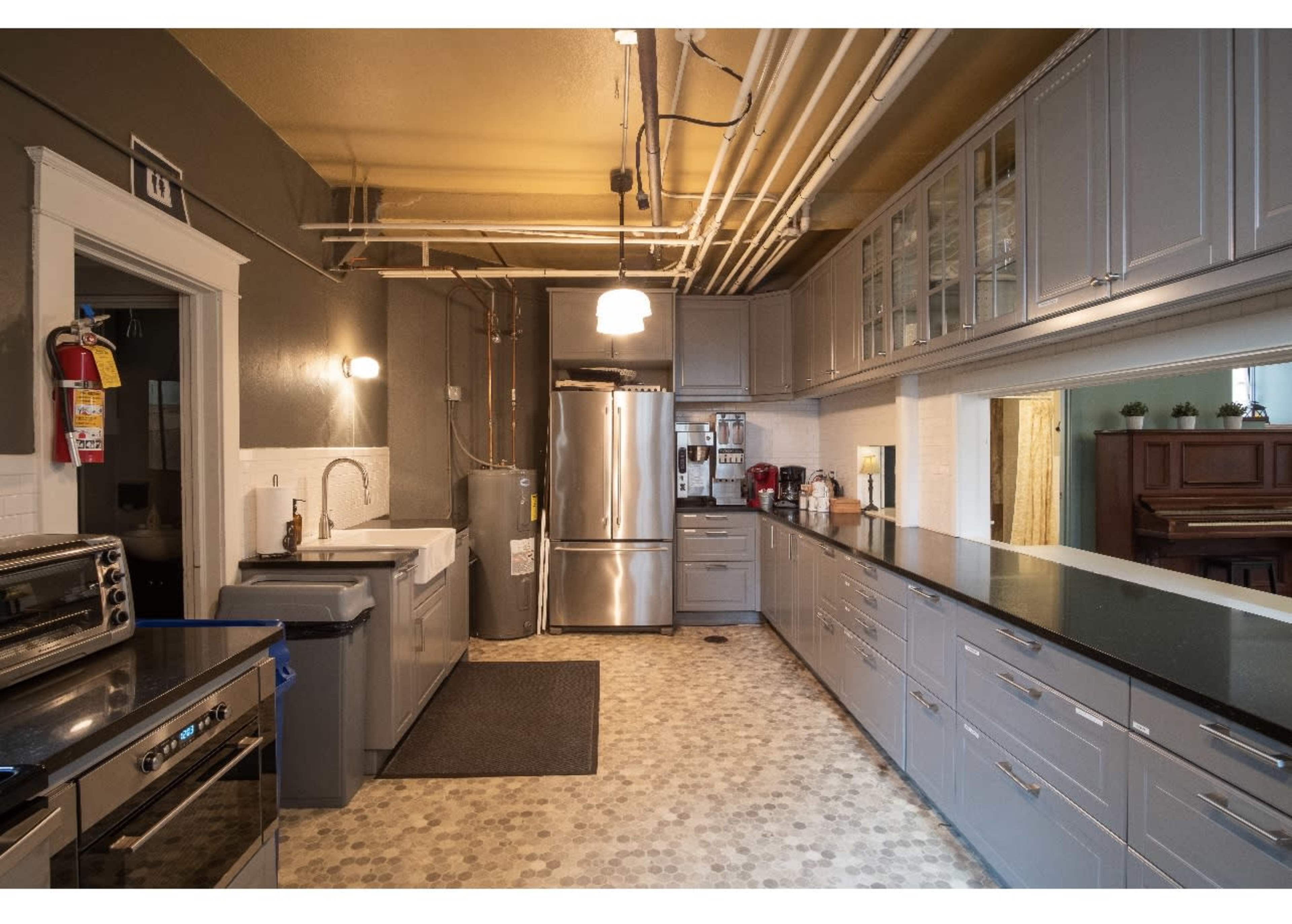 A modern kitchen featuring gray cabinets, stainless steel appliances, a farmhouse sink, and a long counter with a black countertop.