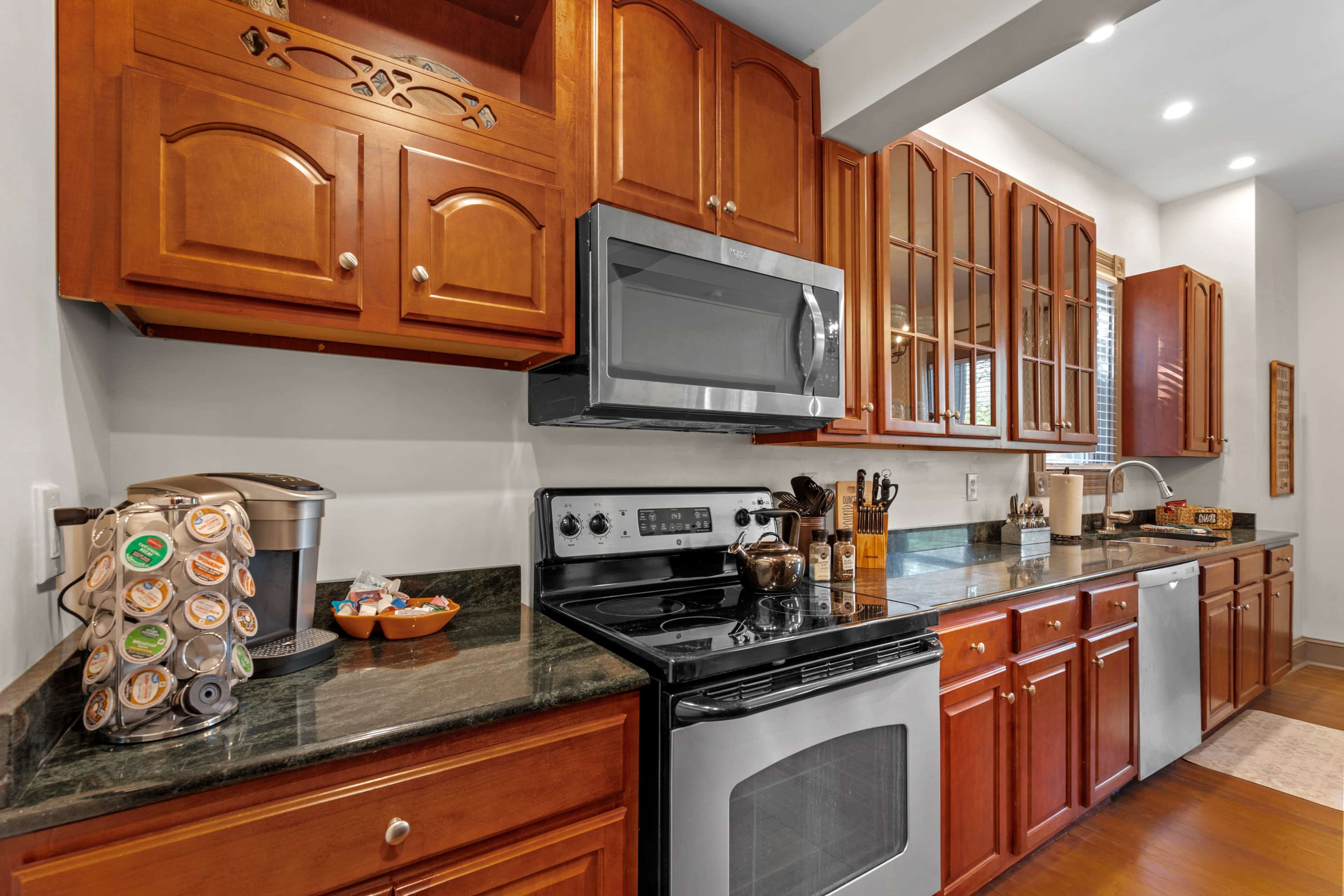 A modern kitchen with wooden cabinets, stainless steel appliances, and a granite countertop featuring a coffee machine and various kitchen items.
