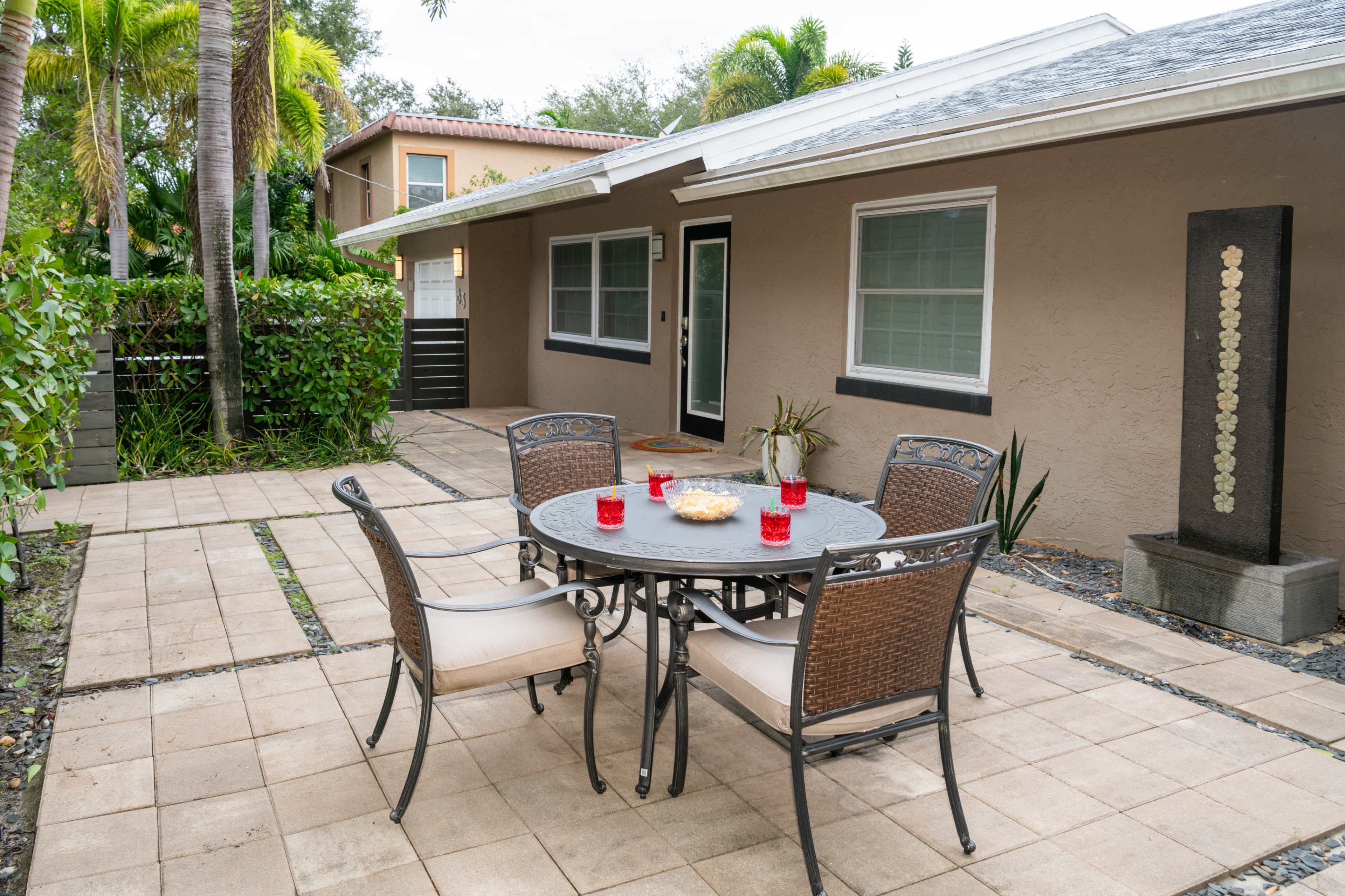 A patio featuring a round table with four chairs, surrounded by concrete pavers and lush greenery.