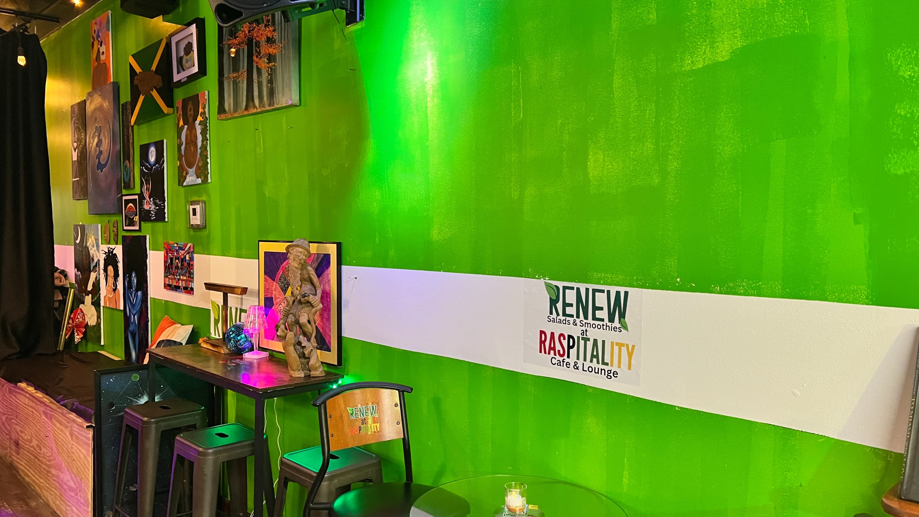 The image shows a vibrant green wall in a café or lounge adorned with various artworks and a sign displaying "RENEW RASPITALITY Cafe & Lounge."