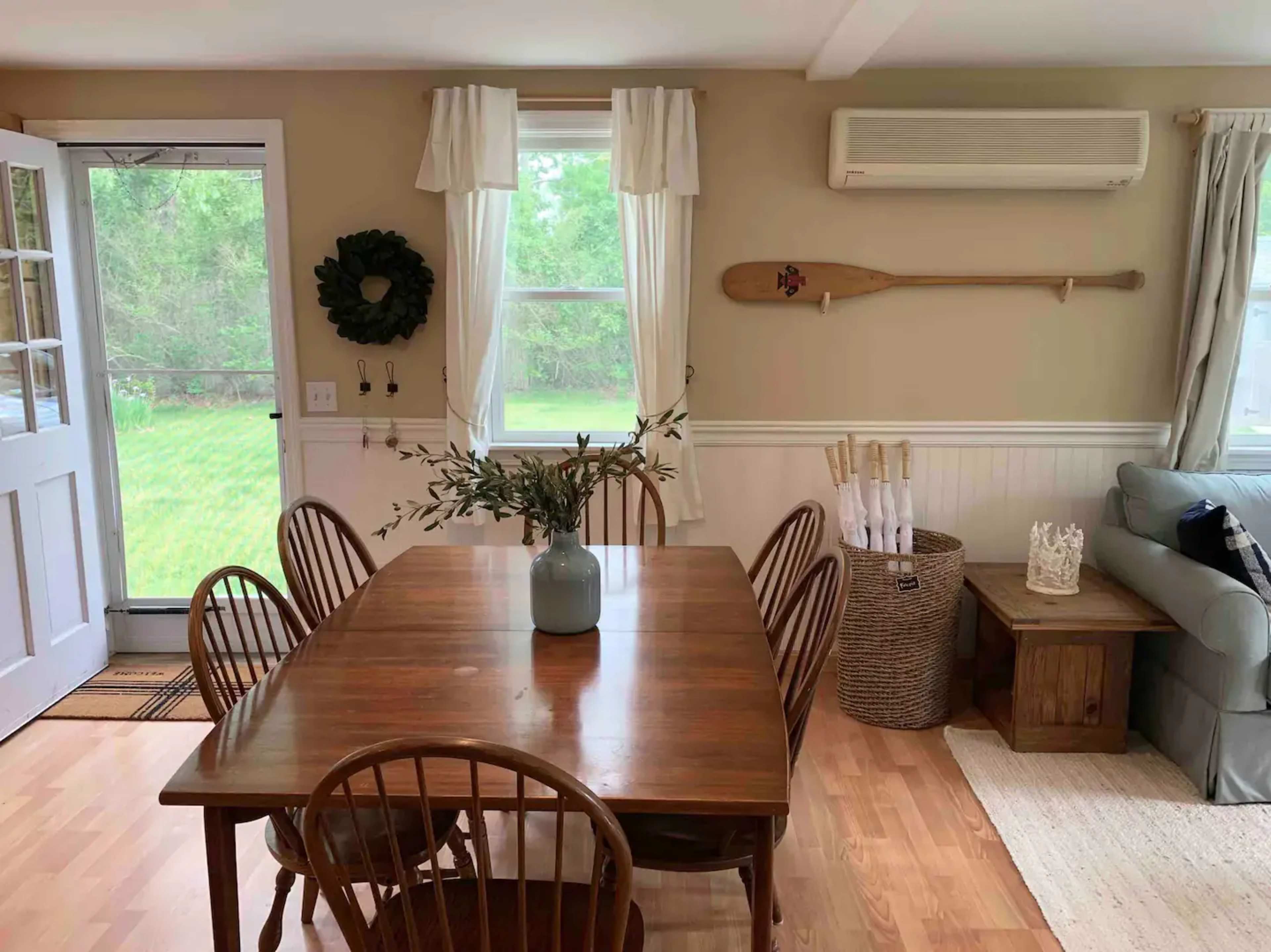 A dining area with a wooden table surrounded by chairs, a vase of greenery on the table, and a sliding door leading to an outdoor space.