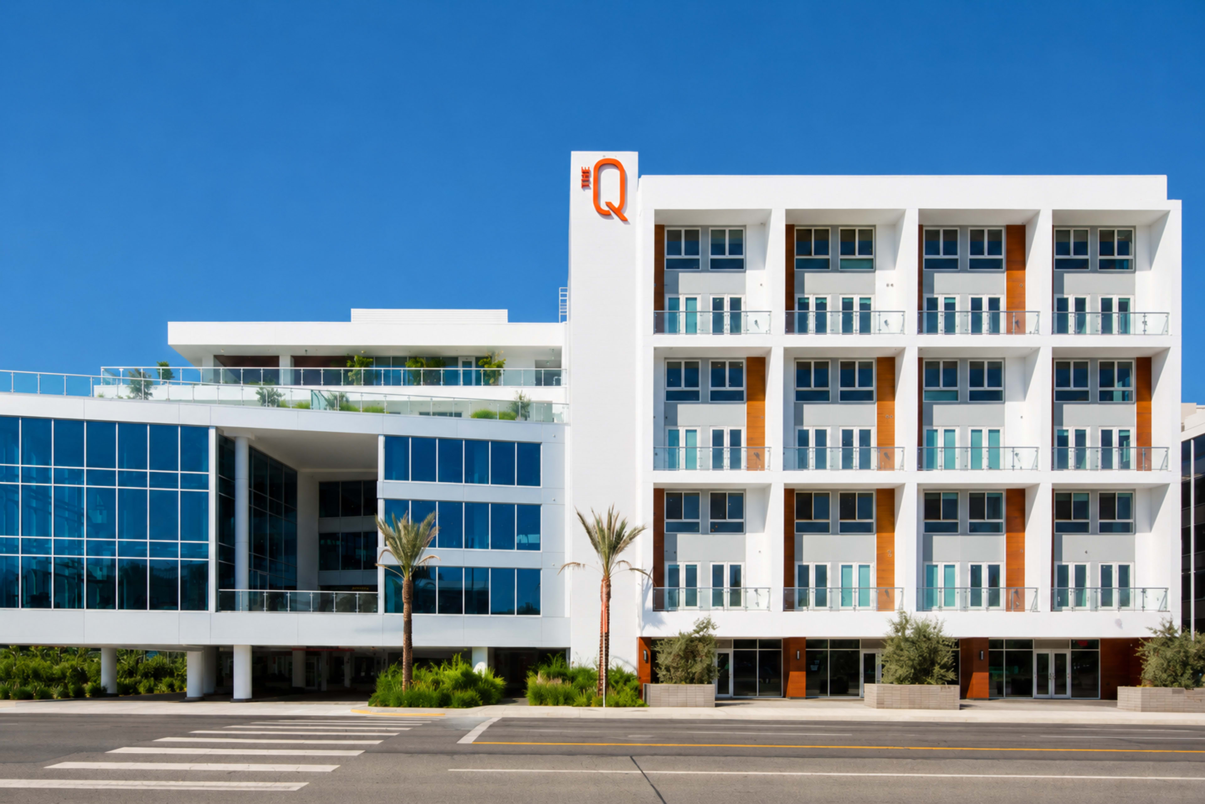 A modern hotel building features large glass windows and multiple balconies, set against a clear blue sky.