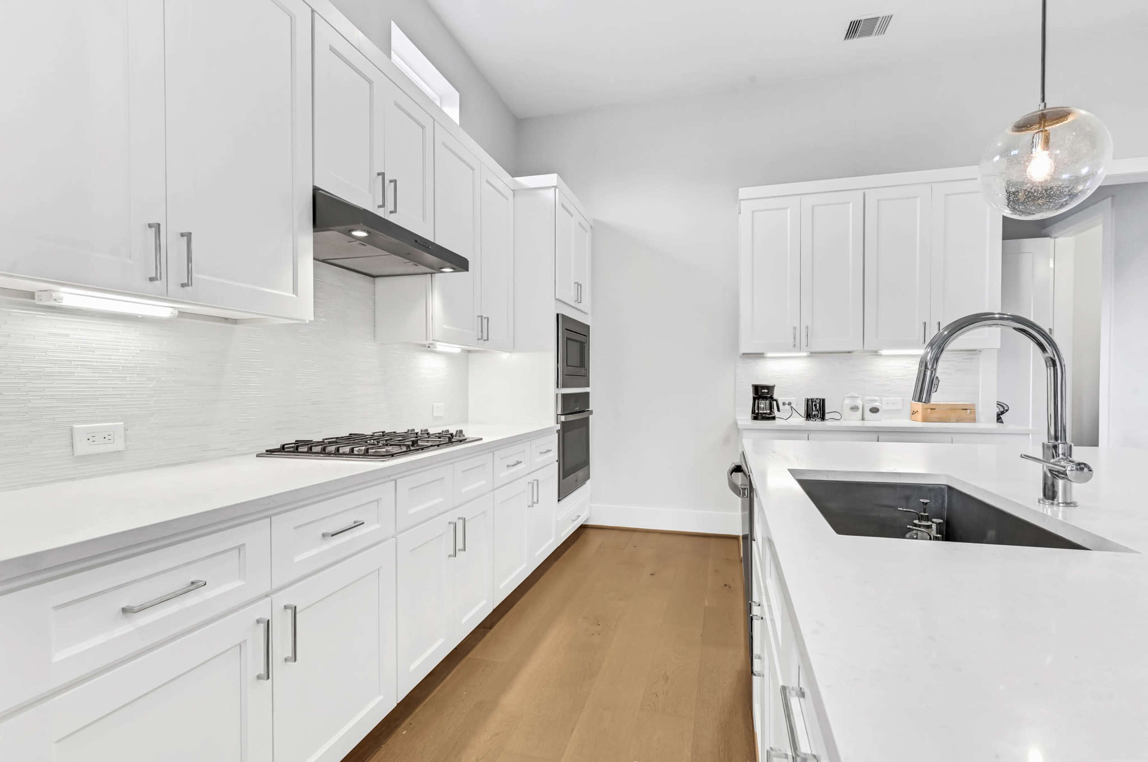 The image shows a modern kitchen with white cabinets, a stainless steel gas stove, and a large island featuring a sink.