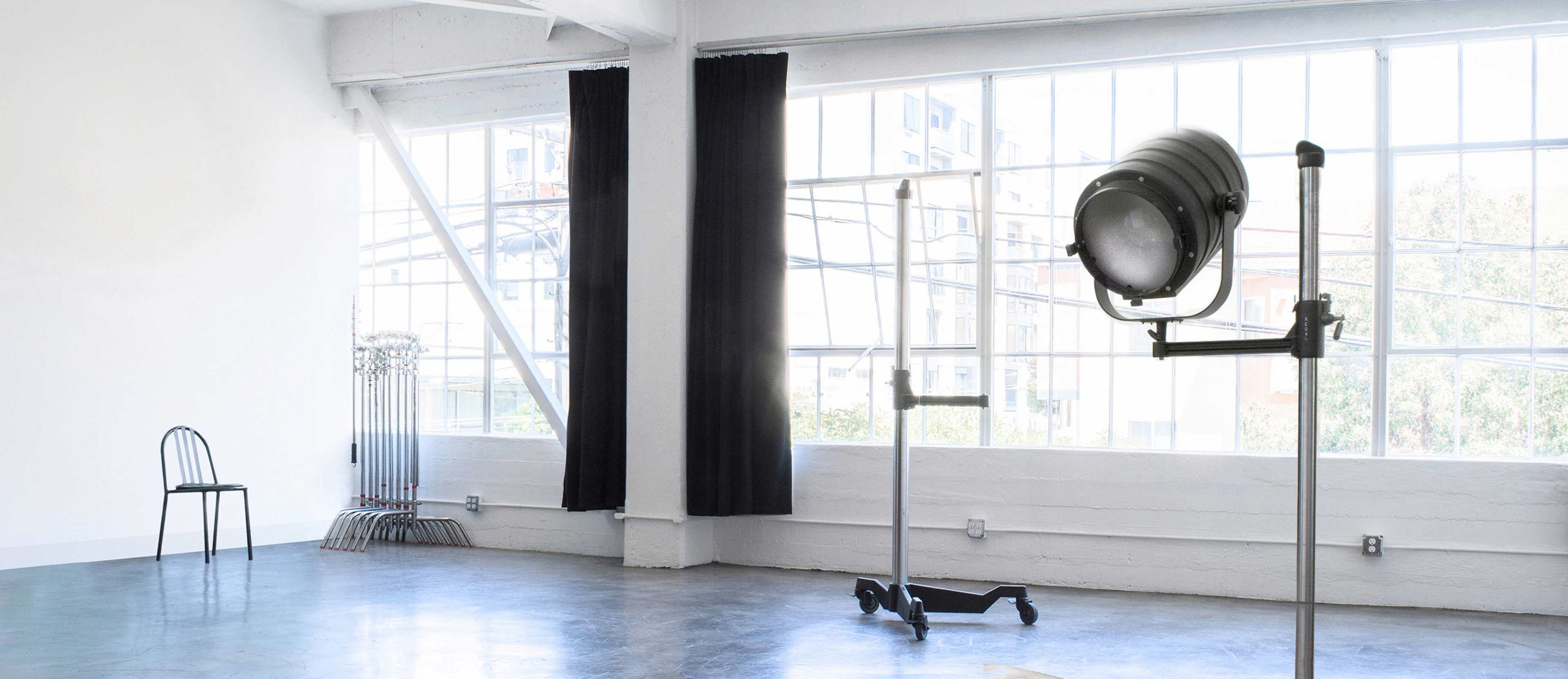 A spacious, minimalist room with large windows, a black chair, and a studio light on a stand.