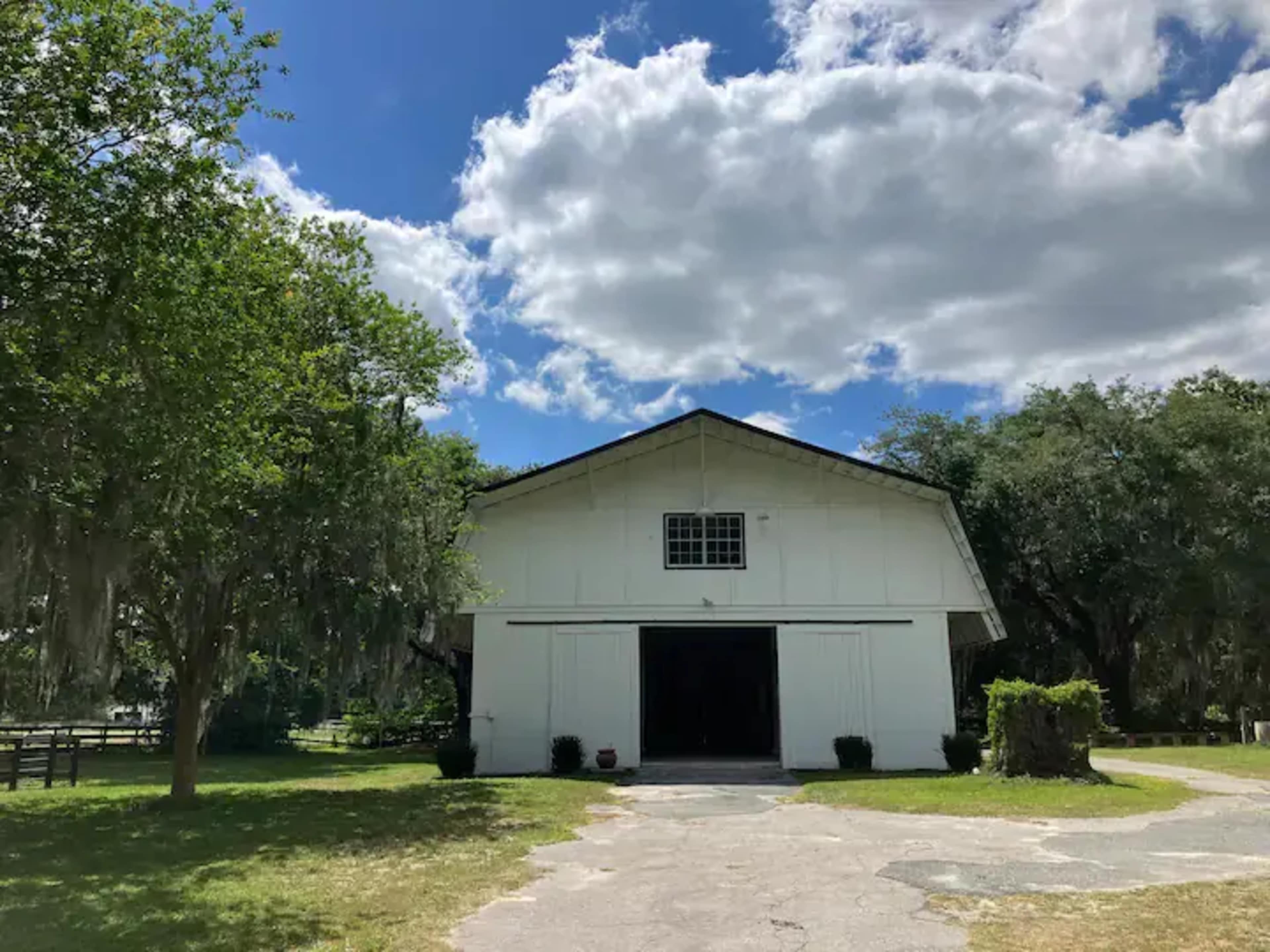 A white barn stands in a grassy area, bordered by trees, under a partly cloudy sky.
