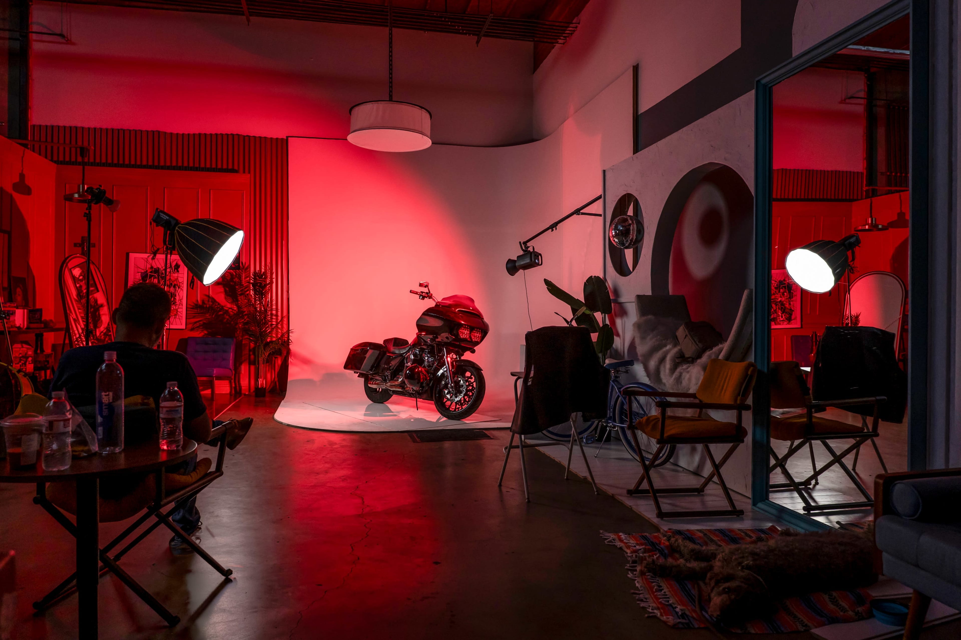 A motorcycle is prominently displayed on a white backdrop illuminated by red lighting in a stylish studio space.