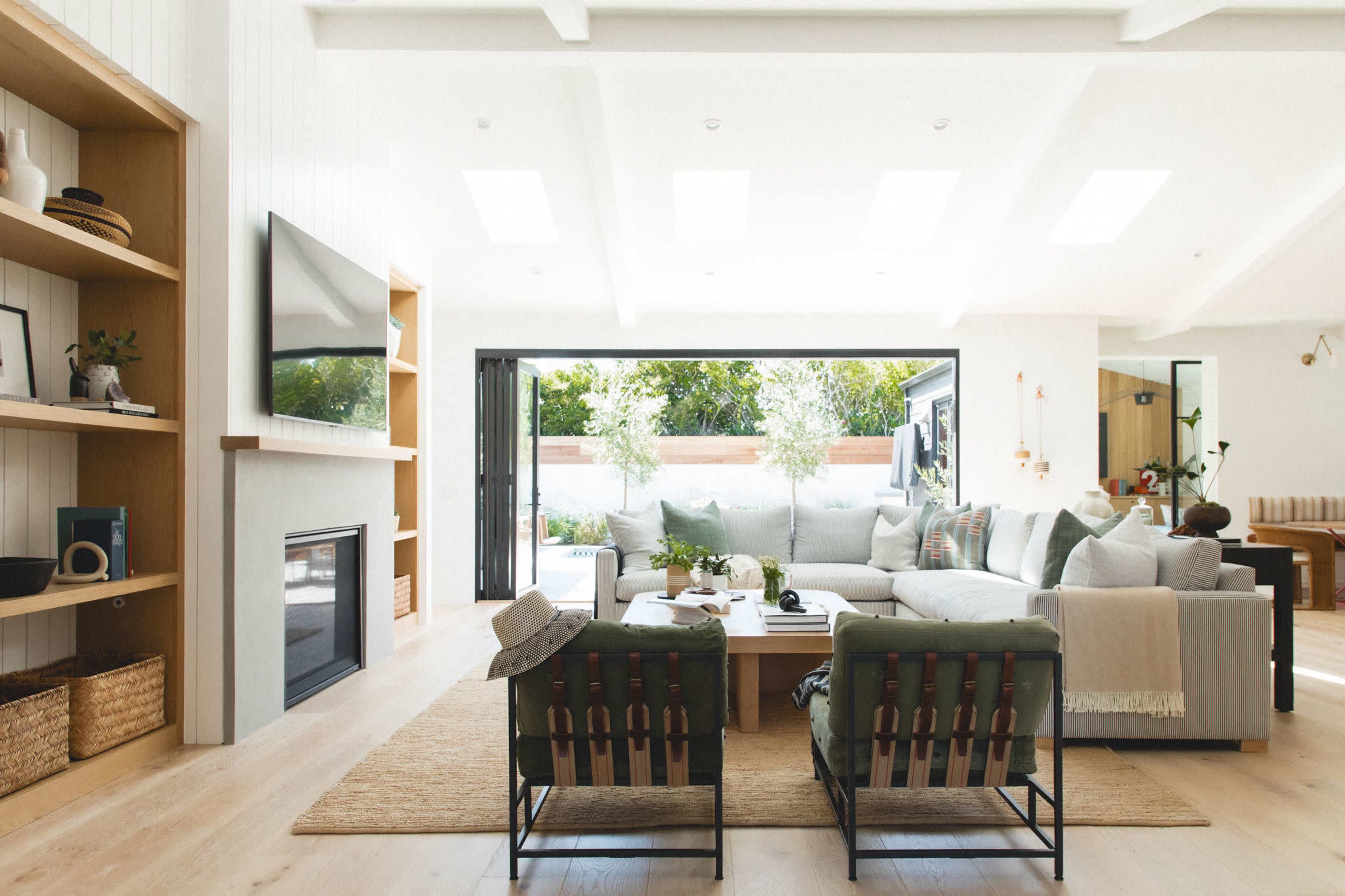 The image shows a modern living room with a large sectional sofa, two green chairs, a coffee table in the center, and sliding glass doors that open to an outdoor area.
