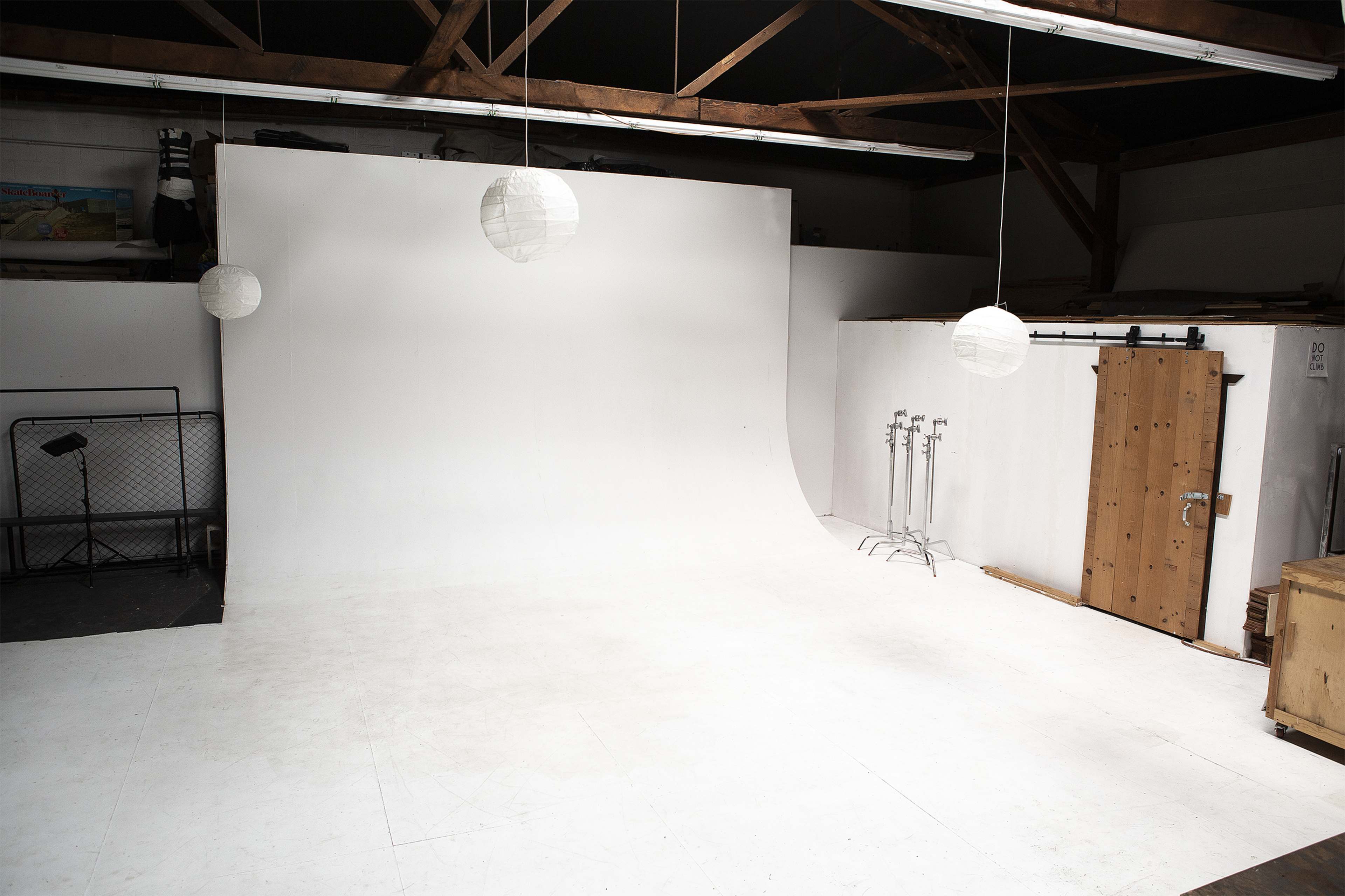 A spacious, empty photography studio with a white backdrop, wooden beams, and several hanging paper lanterns.