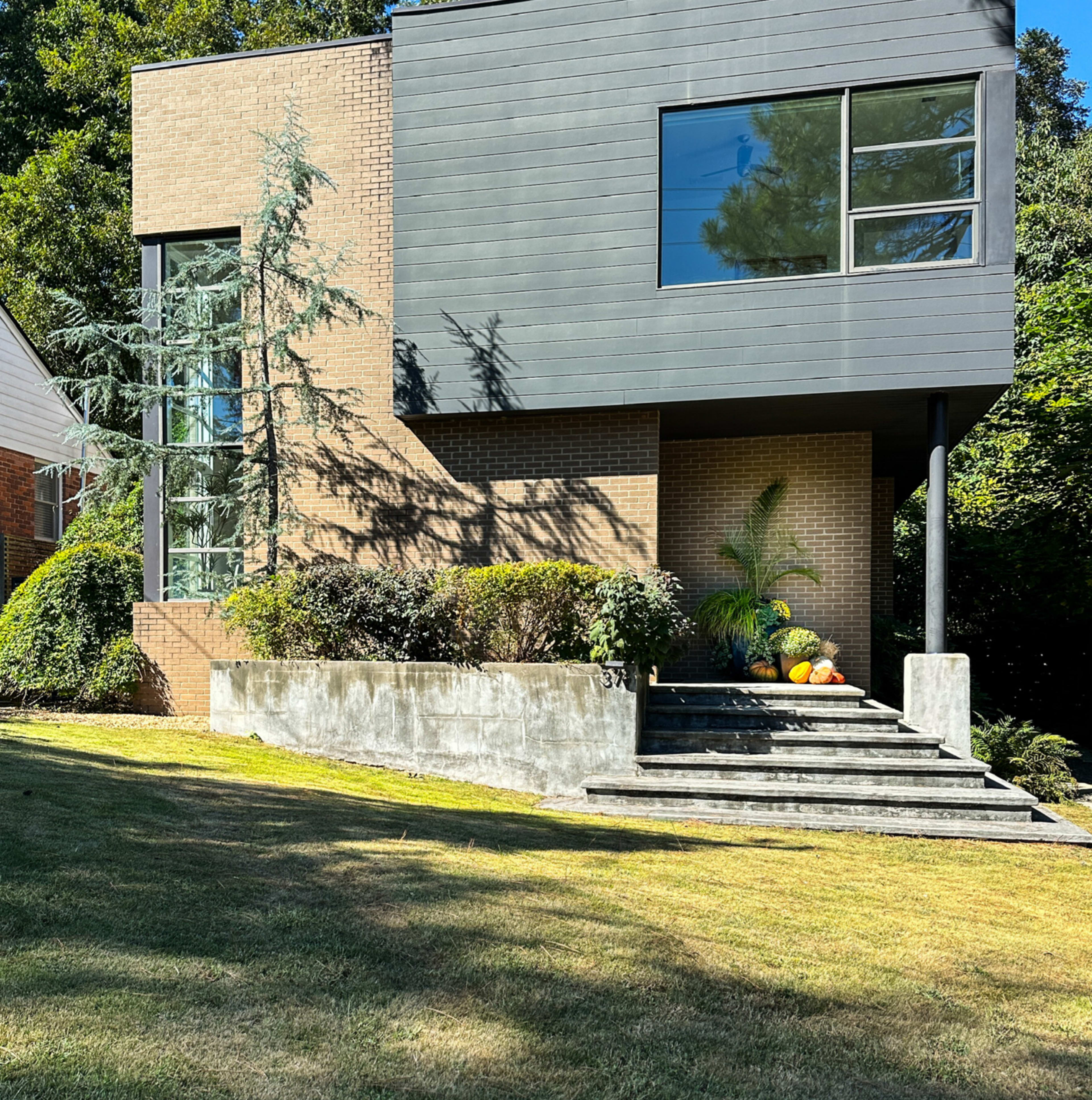 A modern two-story house with a mix of brick and dark paneling features large windows and a landscaped front yard.