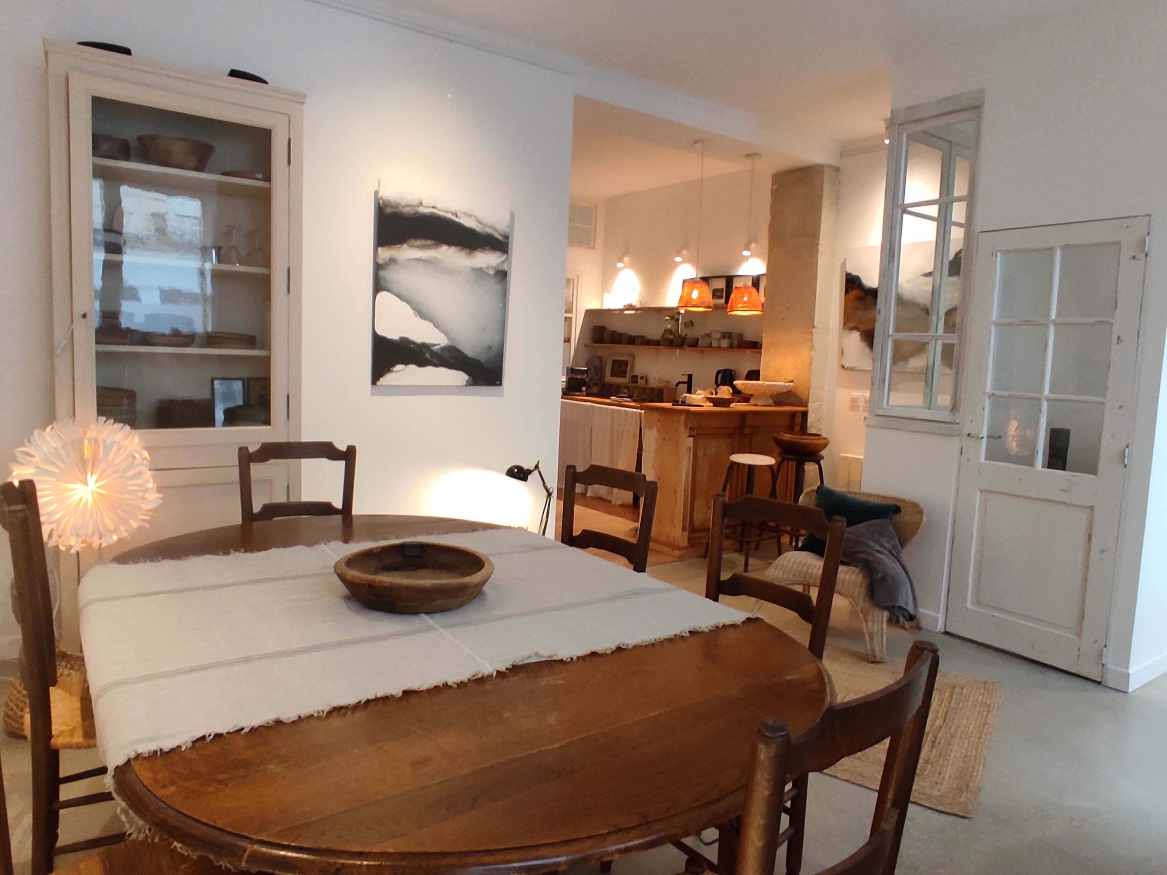 The image shows a dining area with a wooden table and chairs, adjacent to a kitchen and living space featuring warm lighting and contemporary decor.
