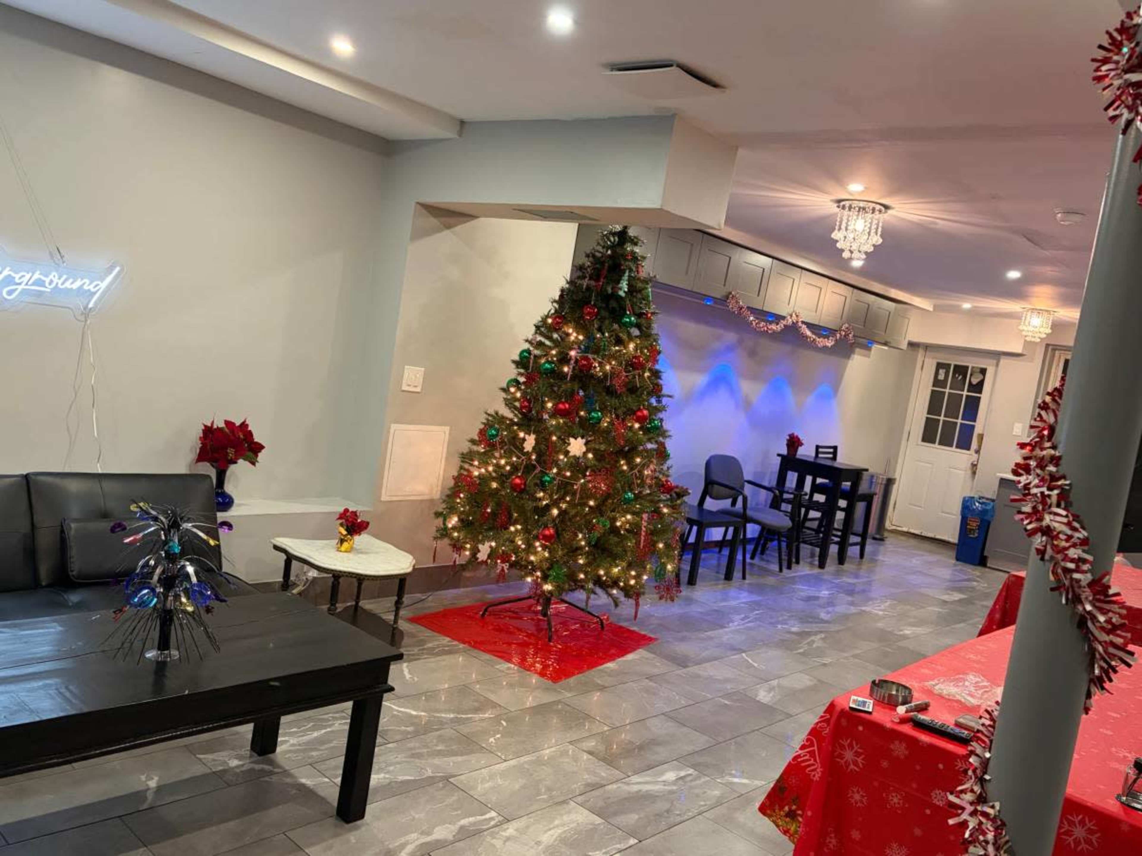 The image shows a decorated interior space featuring a Christmas tree with lights and ornaments, surrounded by festive decor and furniture, including a black couch and tables.