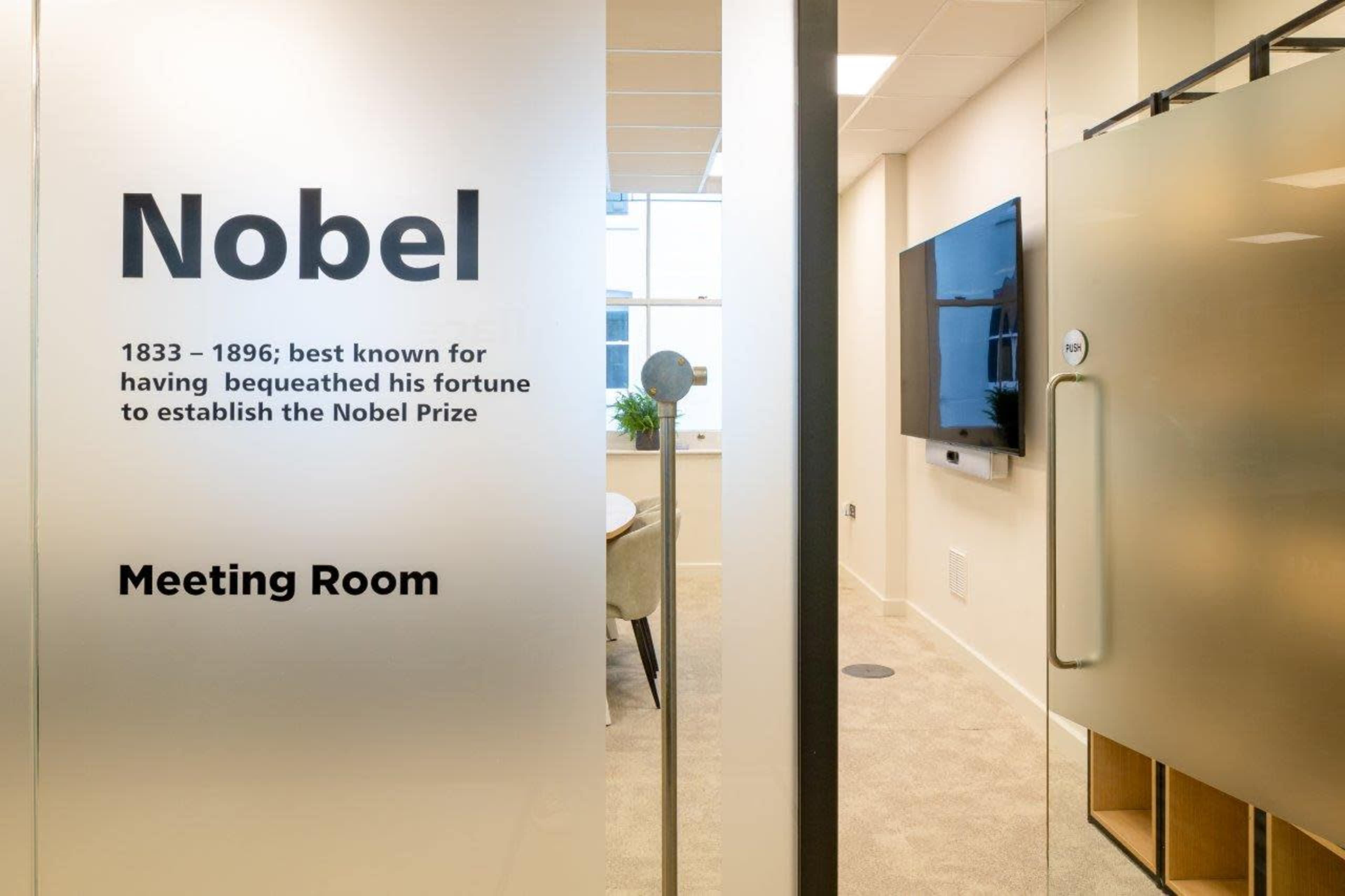 The image shows a conference room door with a frosted glass panel displaying the name "Nobel" and a brief description of Alfred Nobel's contributions along with the words "Meeting Room."