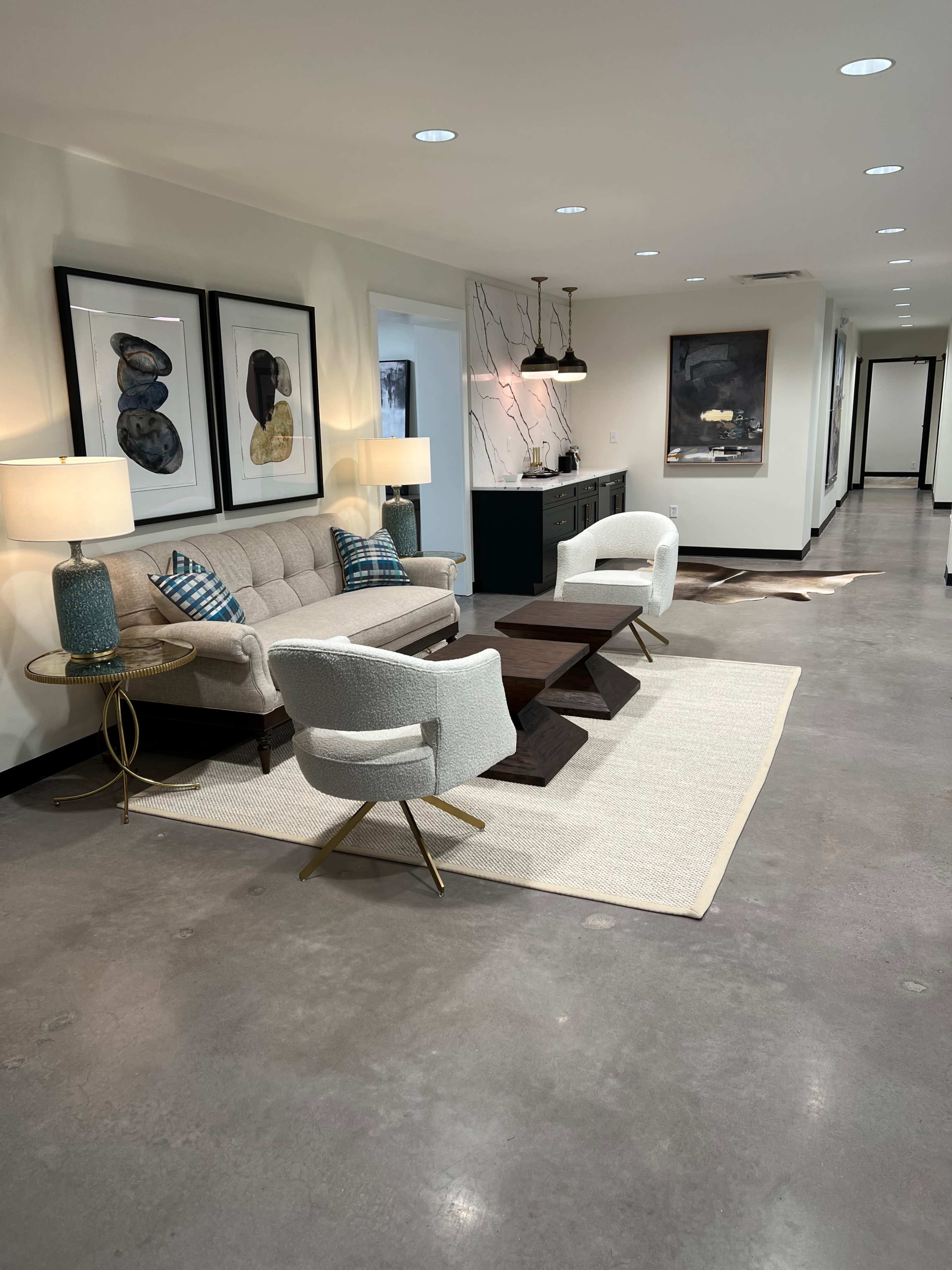 A modern hallway featuring a couch, two armchairs, a coffee table, and decorative wall art, illuminated by overhead lighting.