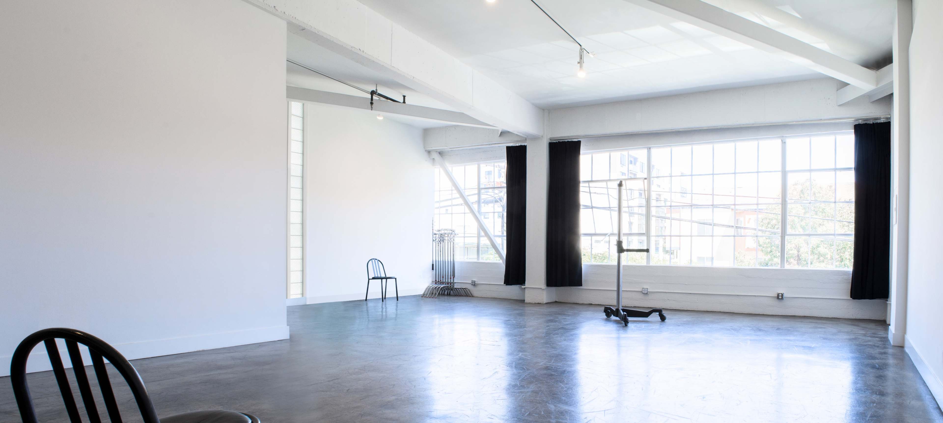 A spacious, well-lit studio with large windows, two black chairs, and a minimalistic design.