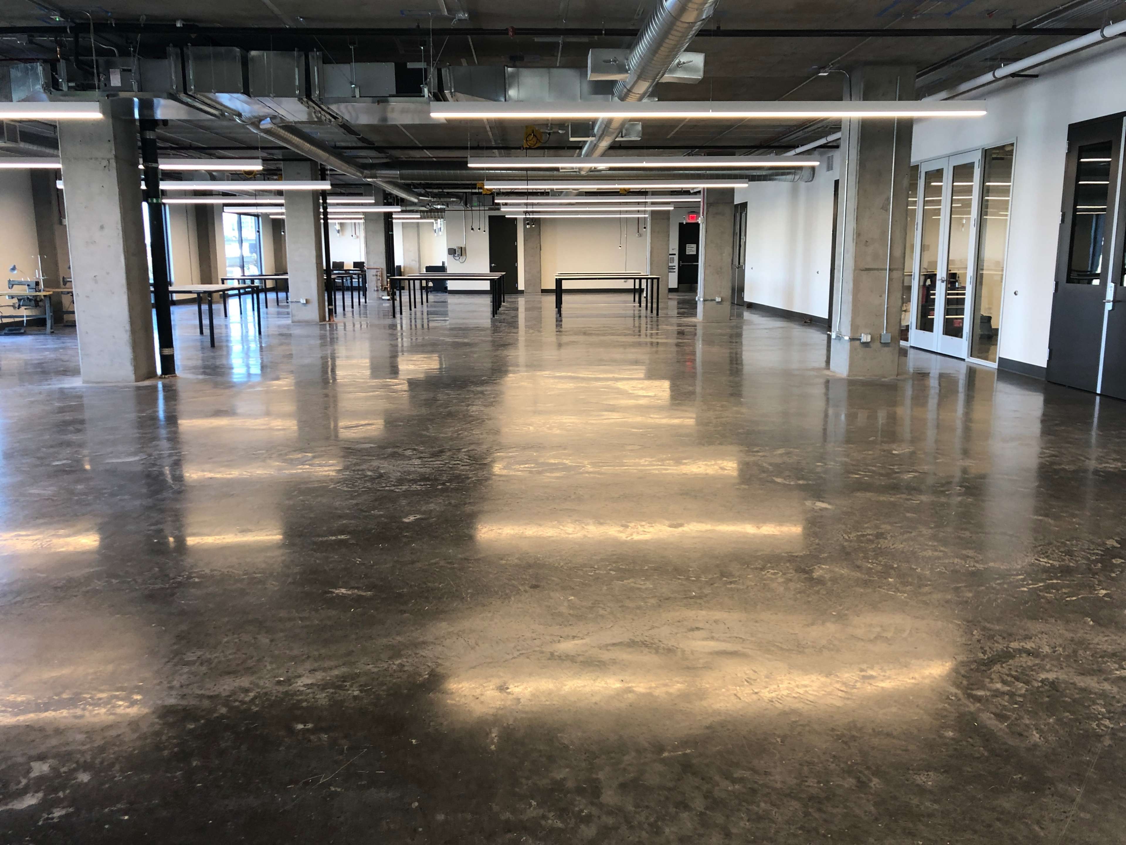 A large, empty industrial-style room with polished concrete flooring and overhead lighting.
