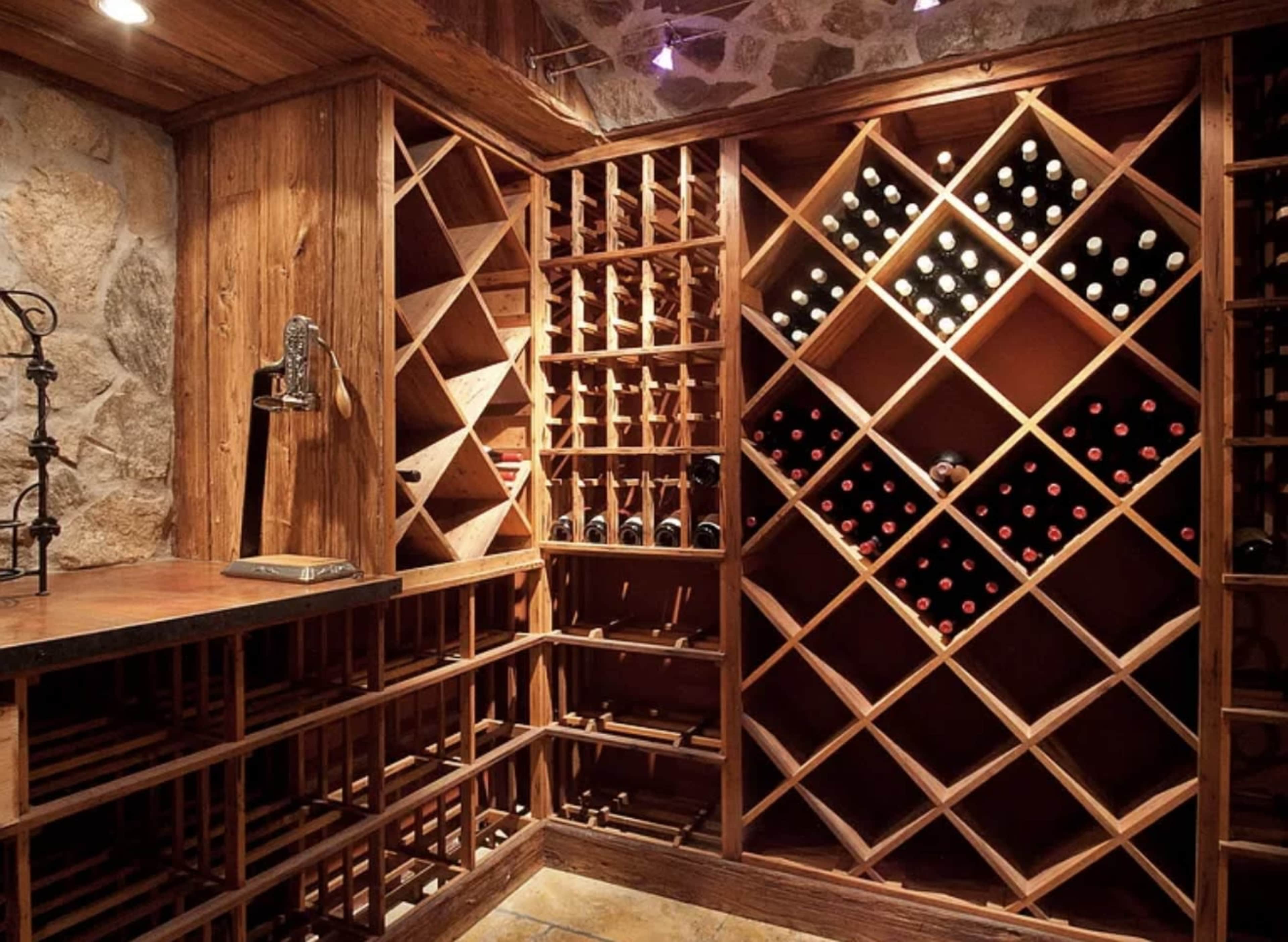 The image shows a wooden wine cellar with neatly arranged wine racks and shelves displaying various bottles of wine.