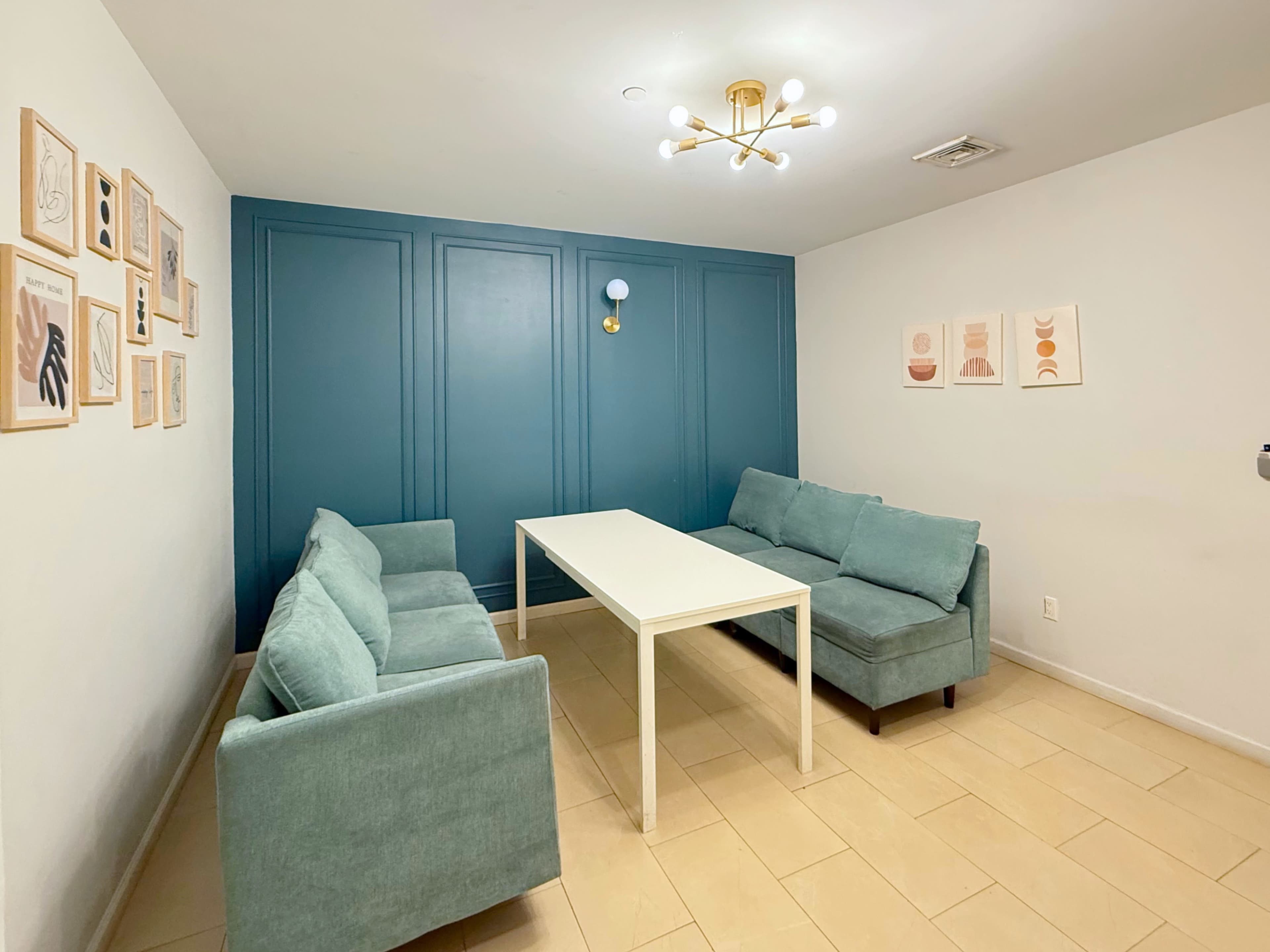 The image shows a small sitting area with two light blue couches and a white table, complemented by framed artwork on the walls.