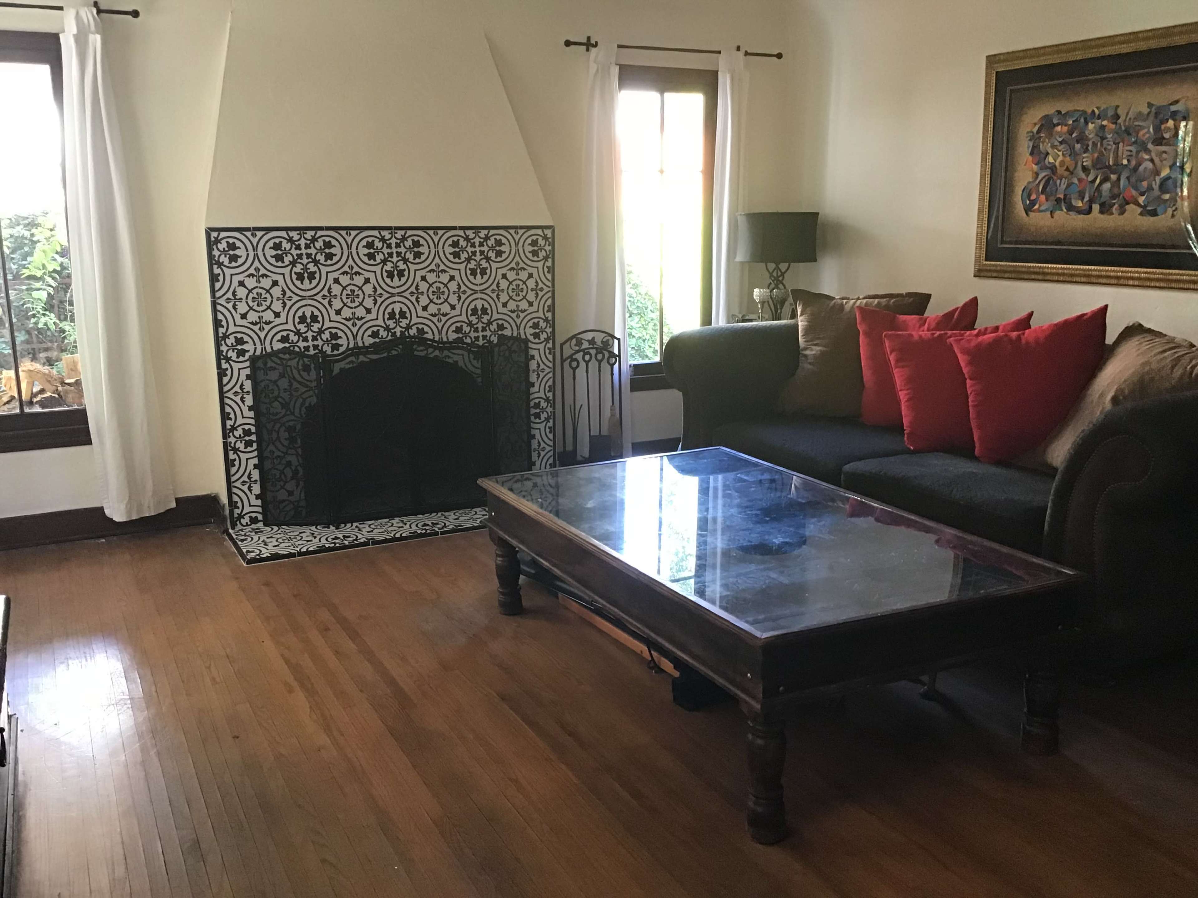 The image shows a living room with a patterned fireplace, a dark couch with red cushions, and a coffee table.
