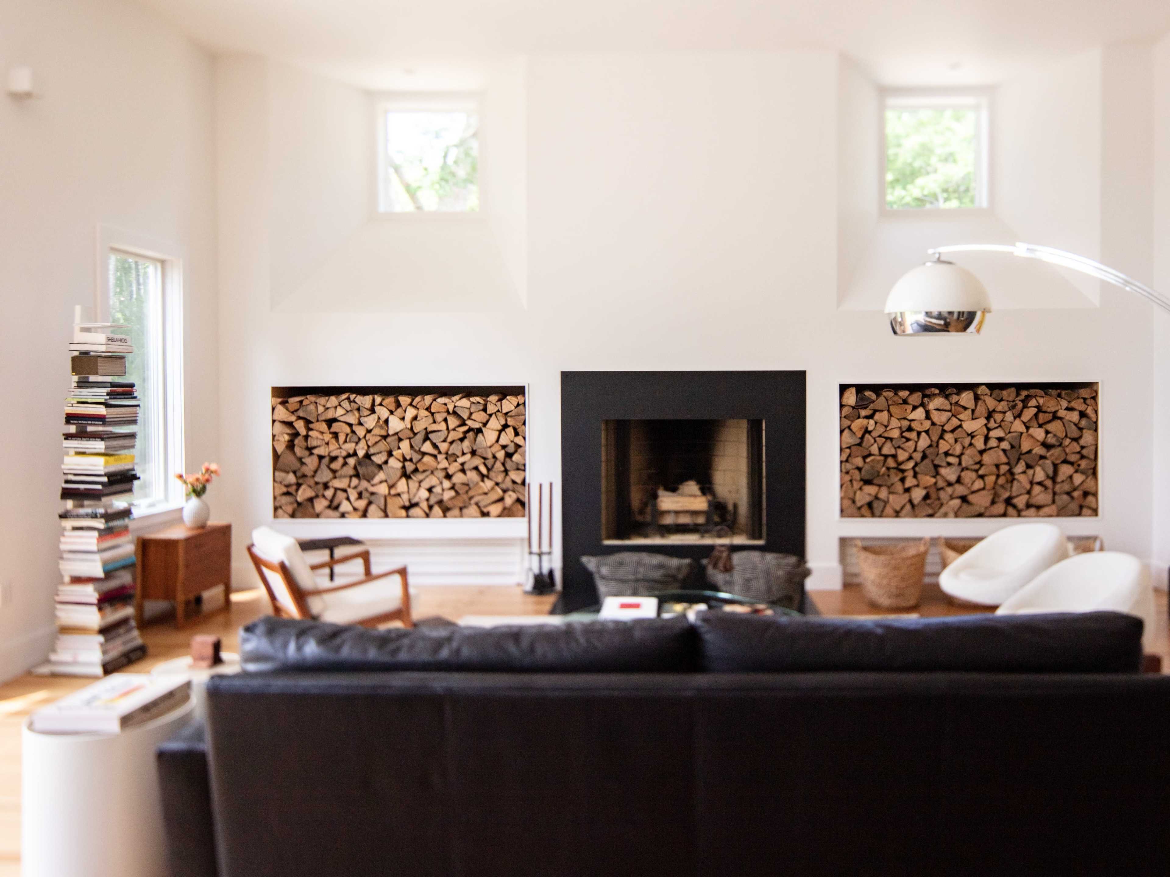 The living room features a black sofa facing a fireplace with stacked wood on either side and a modern lamp beside it.