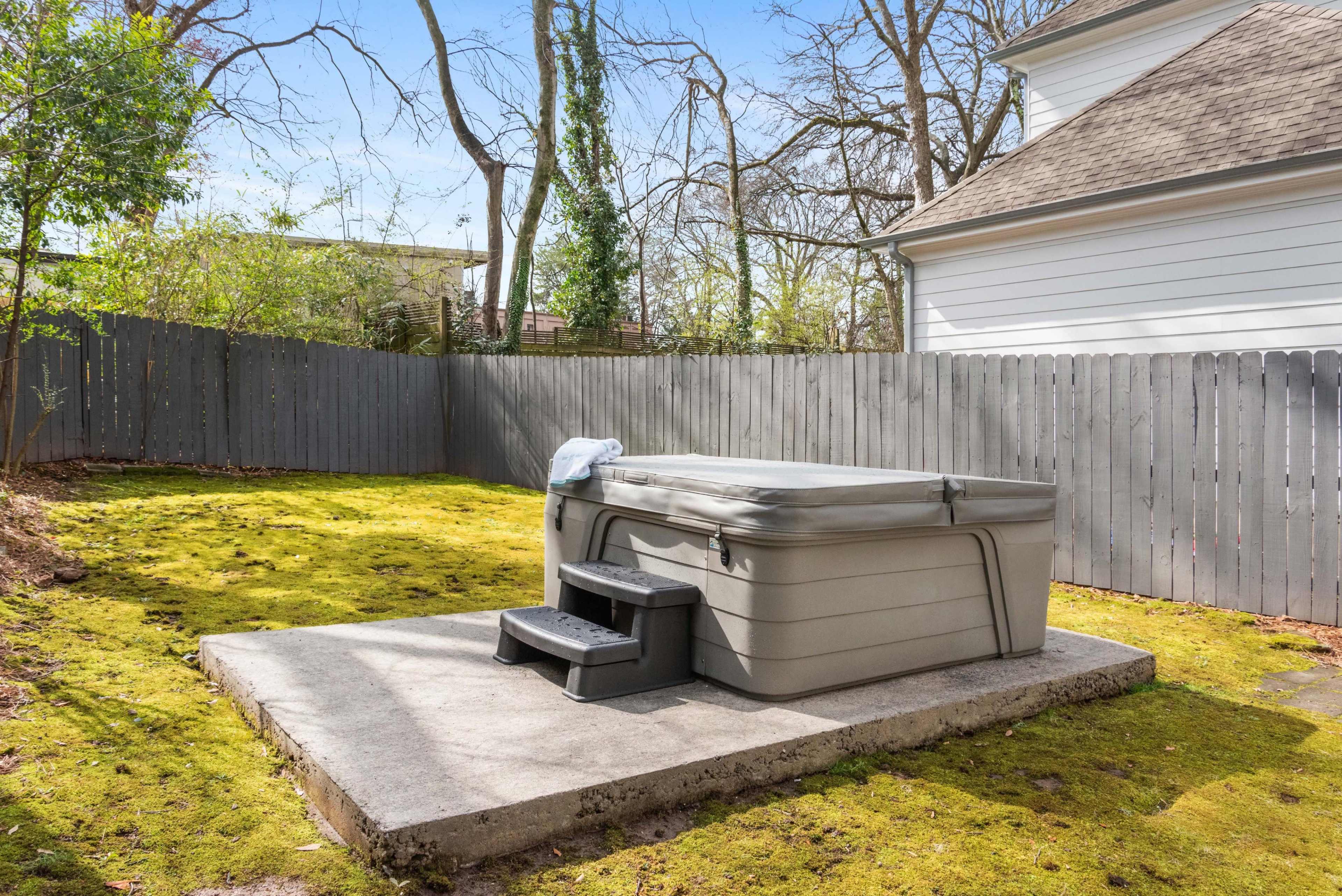 A hot tub with steps is situated on a concrete slab in a grassy backyard surrounded by a wooden fence.