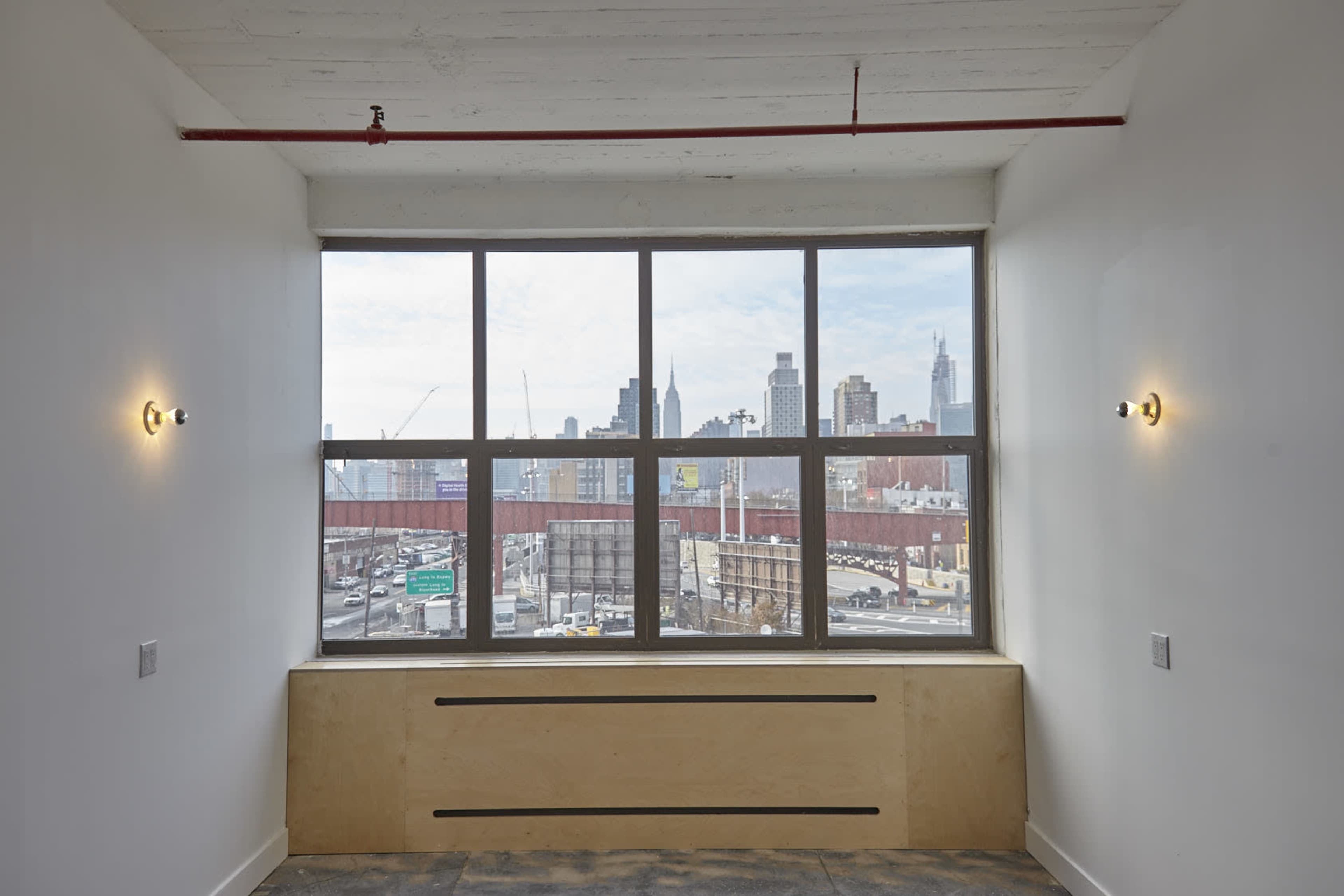 A room with large windows offers a view of a city skyline and a highway below.