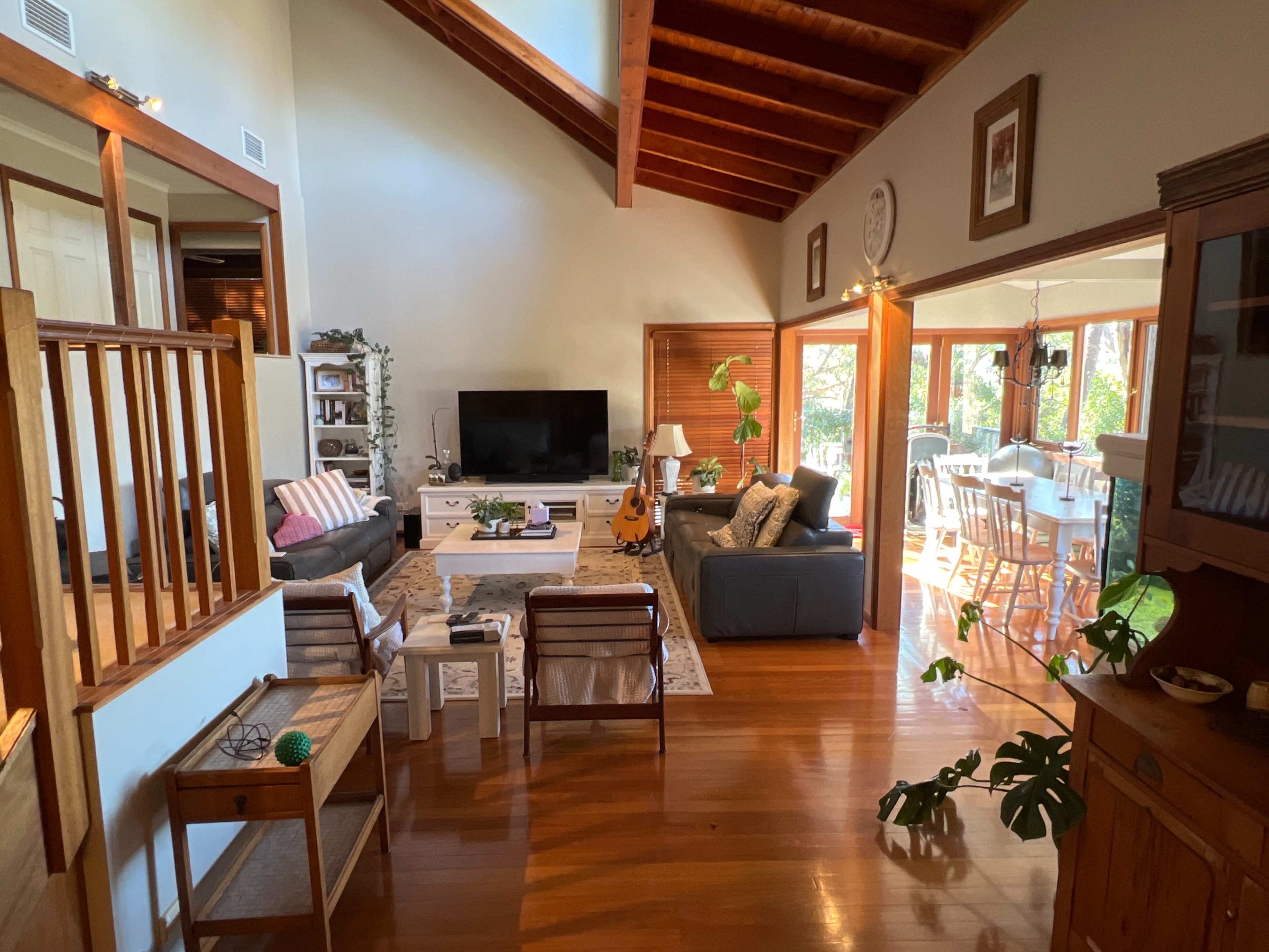 A spacious living room features a large television, comfortable seating, and a dining area with a view of the outdoors.