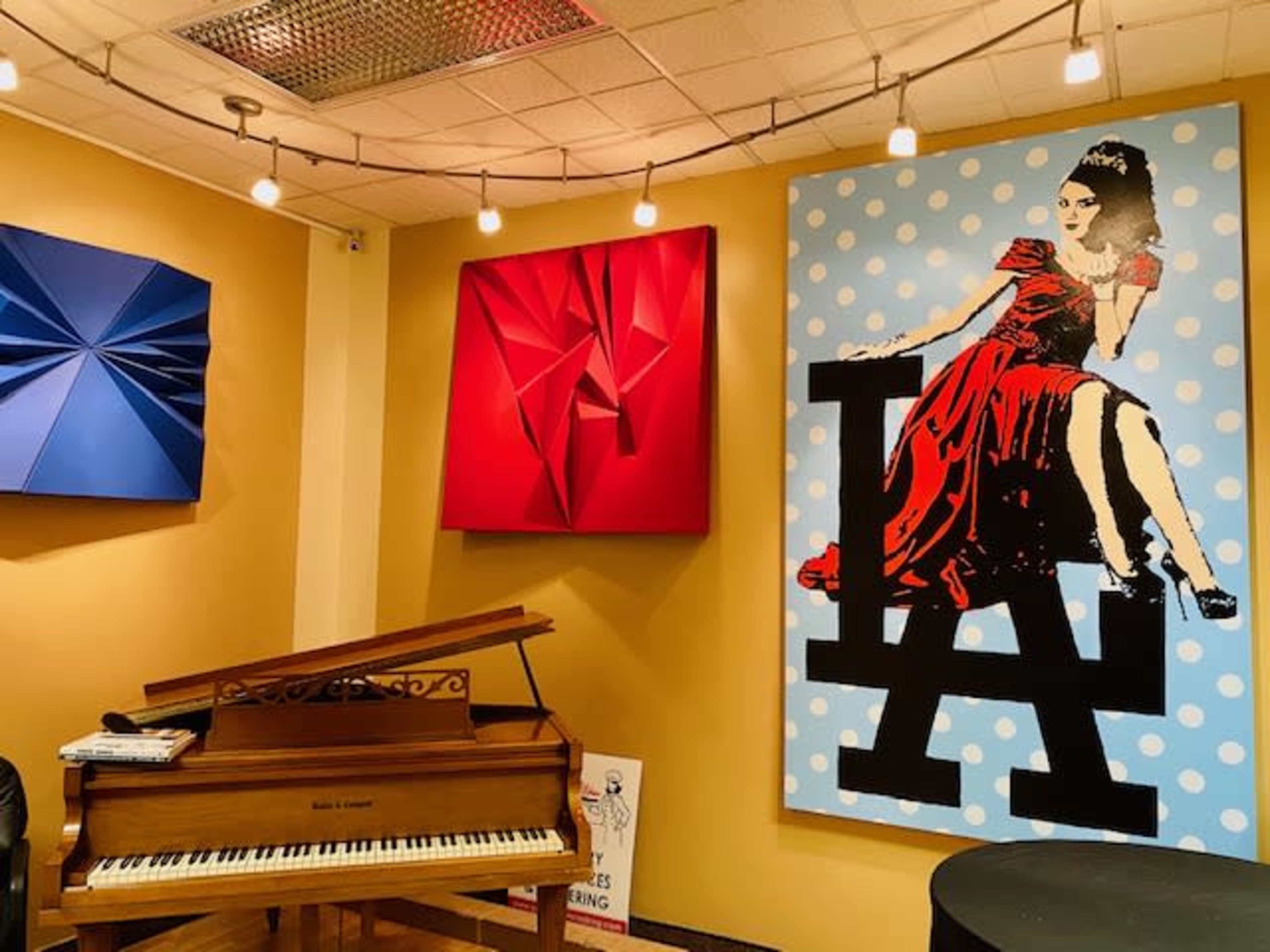The image shows a music room featuring a grand piano, vibrant wall art, and decorative lighting.