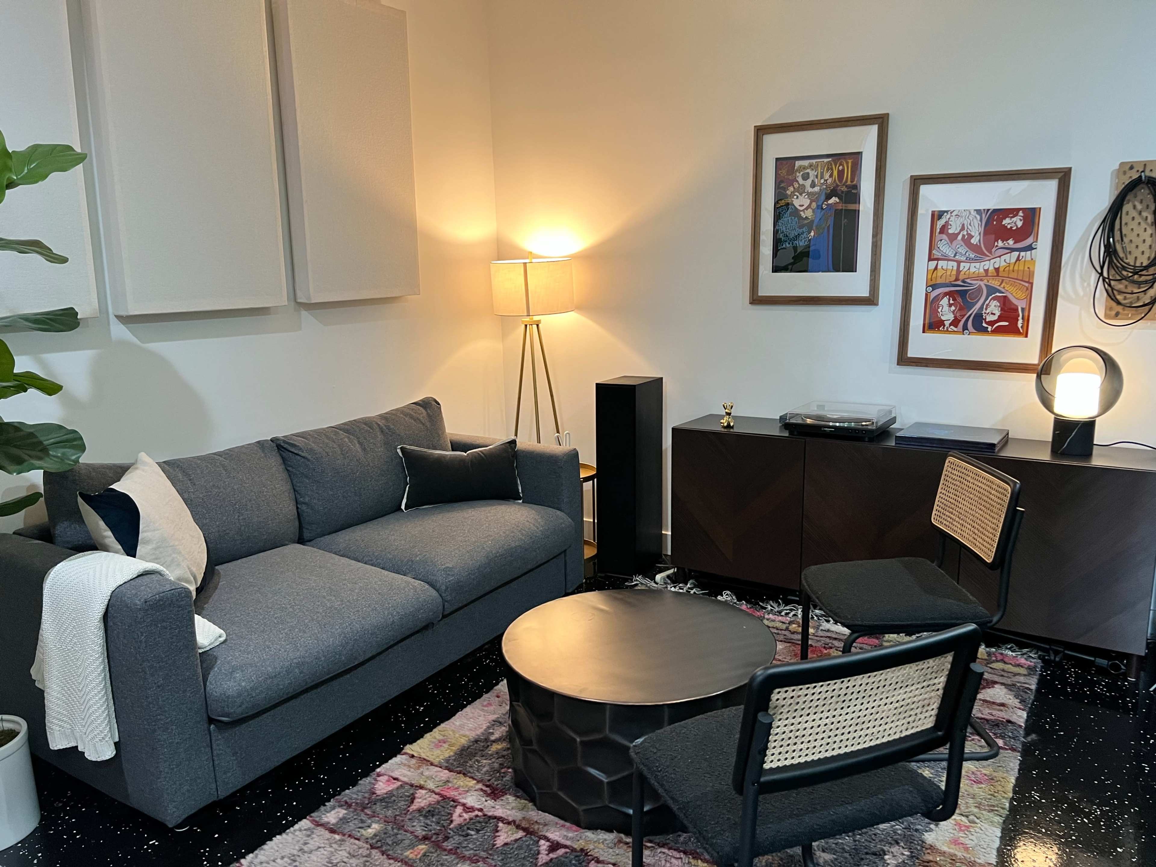 A modern living room with a gray sofa, a round coffee table, two chairs, and framed artwork on the walls, illuminated by a floor lamp.