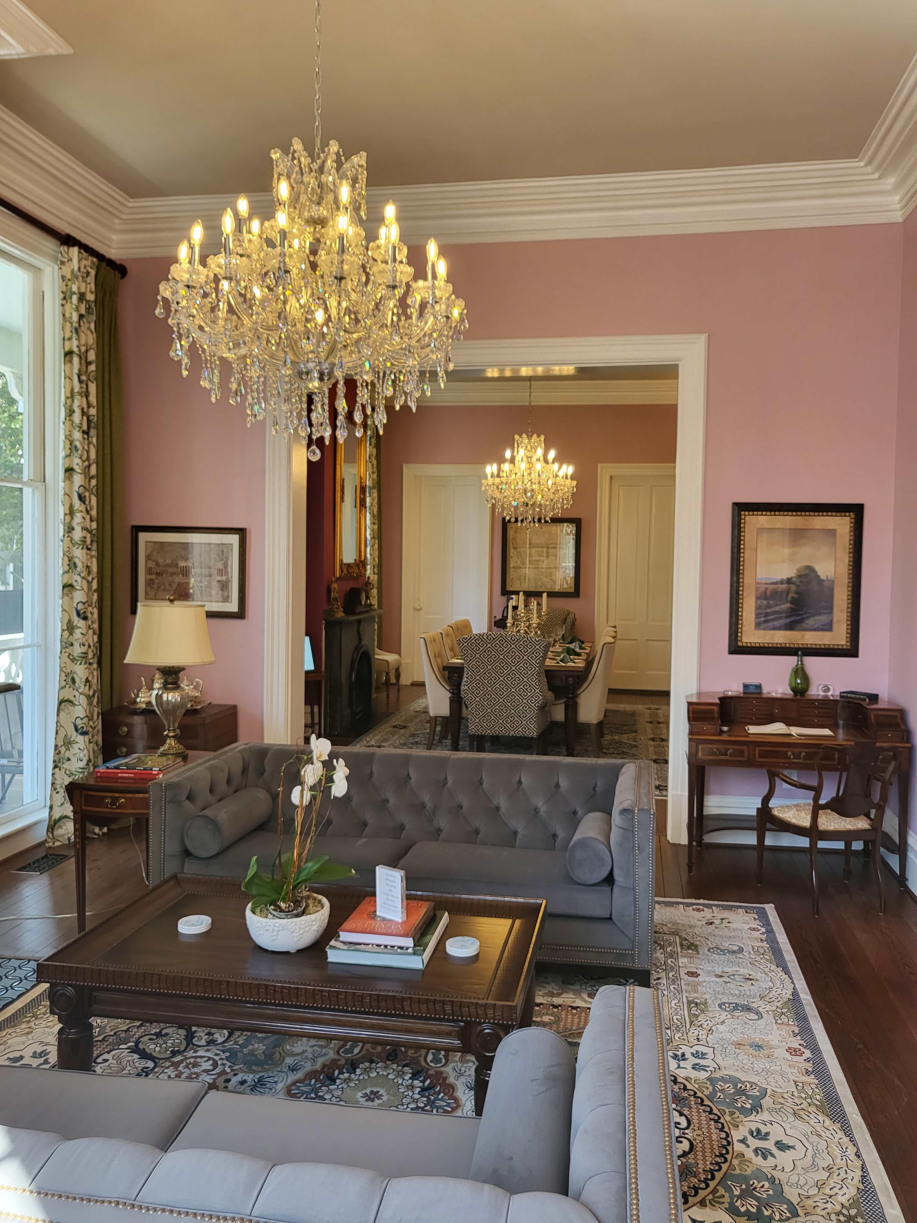 A well-furnished living room with a large chandelier, a coffee table, and a view of an adjacent dining area through an open doorway.