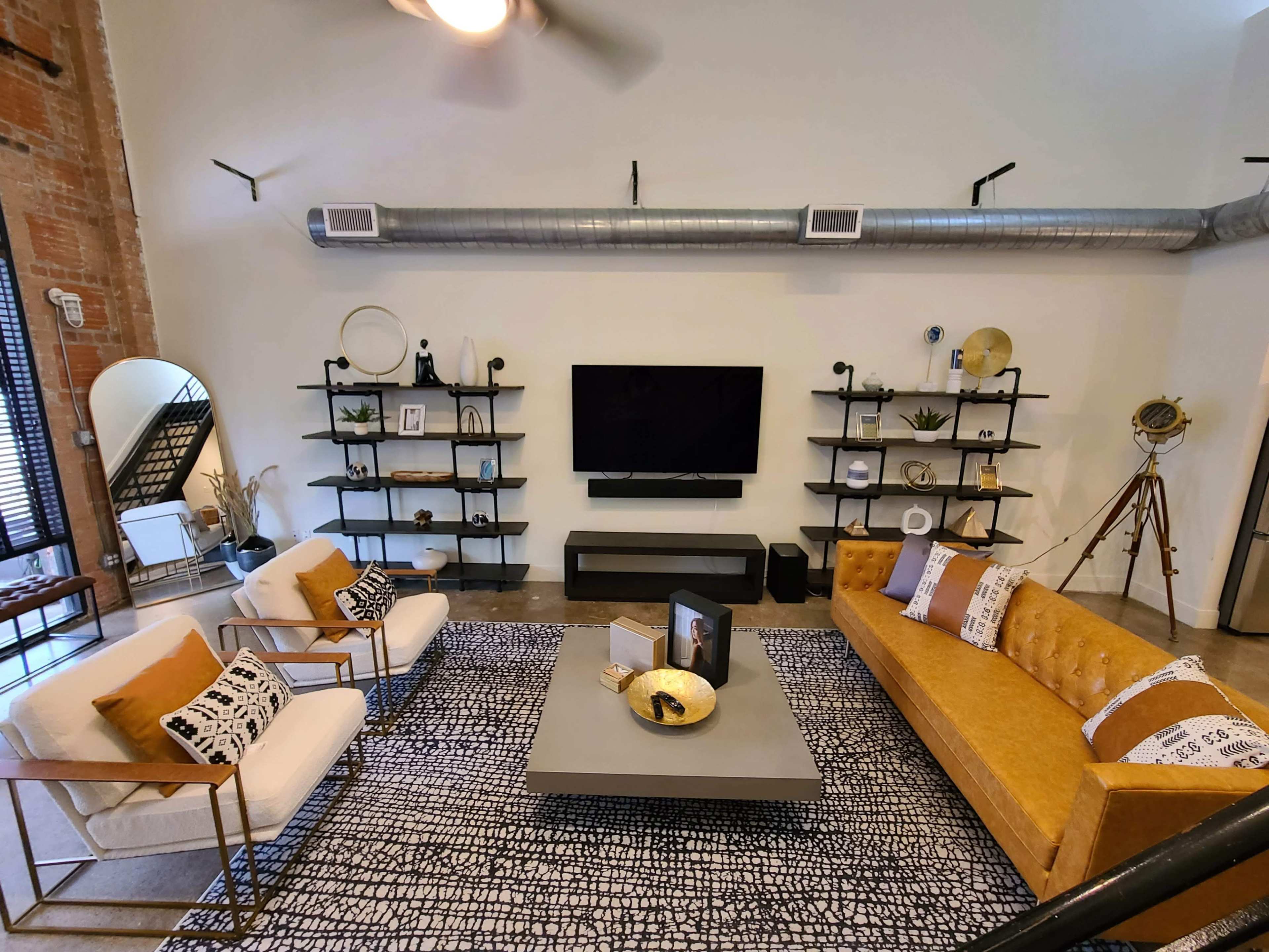 A modern living room featuring two couches, a coffee table in the center, and shelving units with decorative items, all set against a backdrop of exposed brick and industrial-style elements.