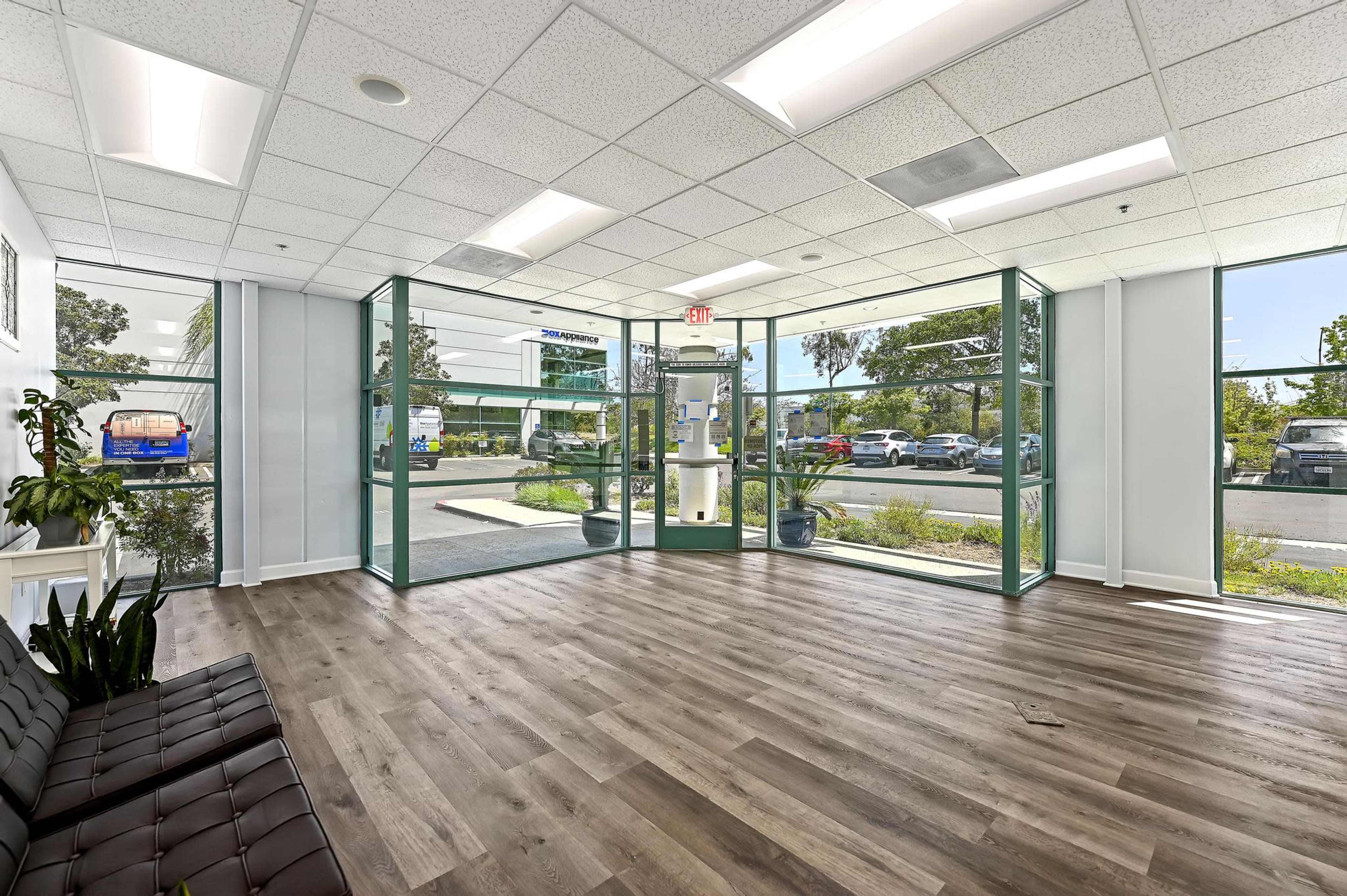A modern office lobby with large glass windows, wooden flooring, and a seating area.