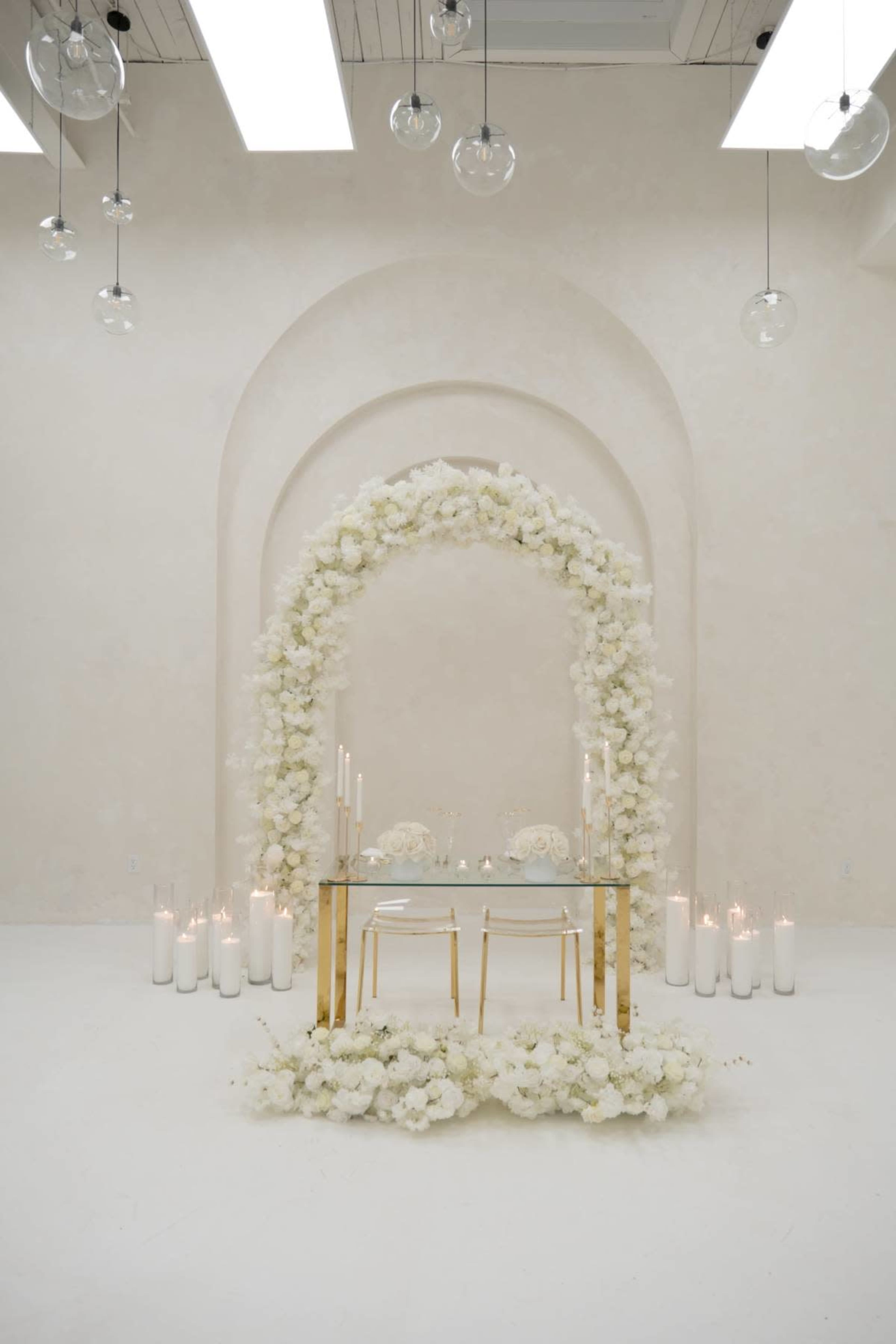 A minimalist wedding altar is adorned with white flowers and candles, set against a softly lit, neutral backdrop.