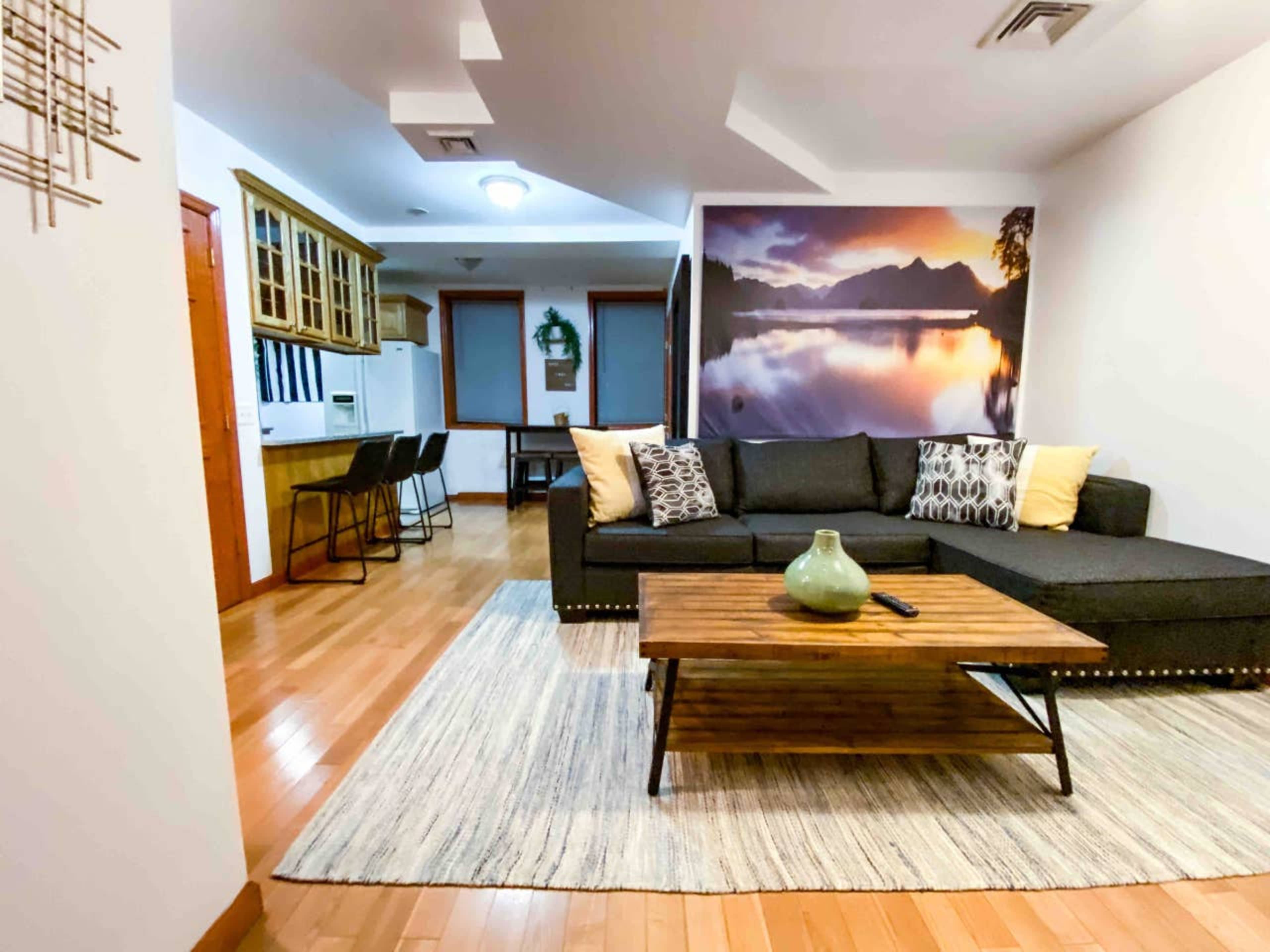 A modern living room with a sectional sofa, a wooden coffee table, and a wall featuring a scenic mountain and lake mural.