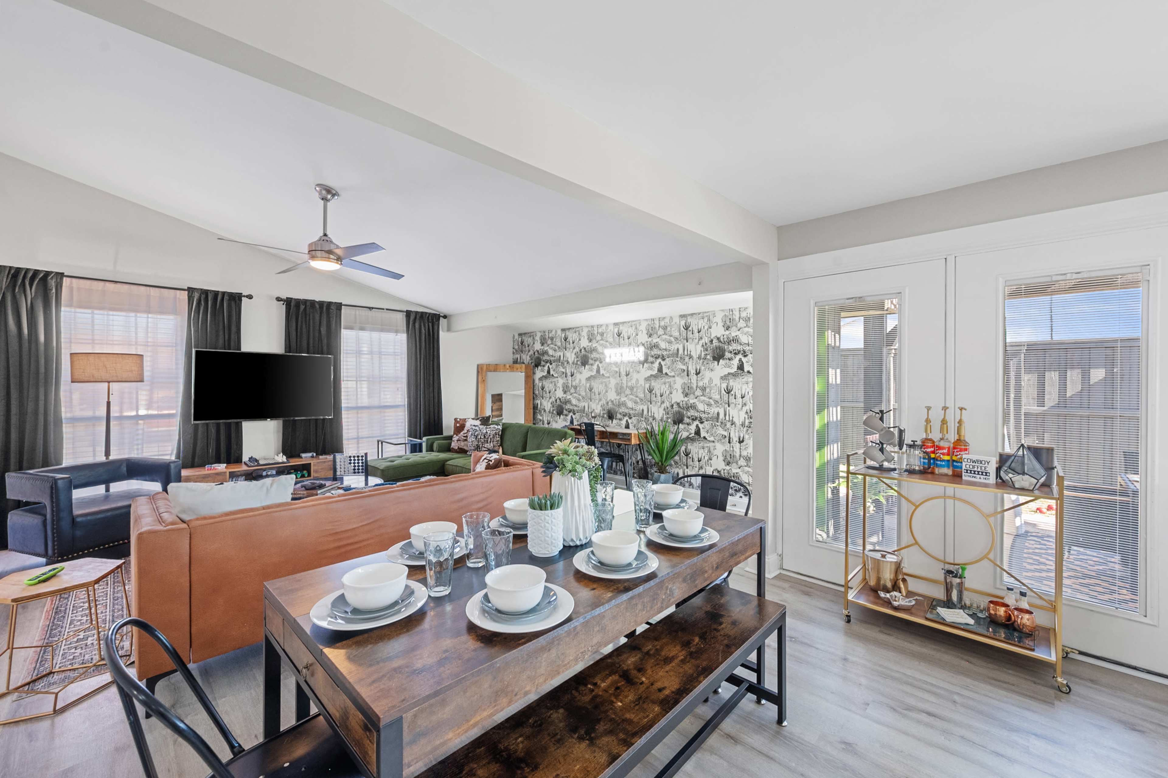 A modern living room with a seating area, a wall-mounted television, and a dining table set for a meal.