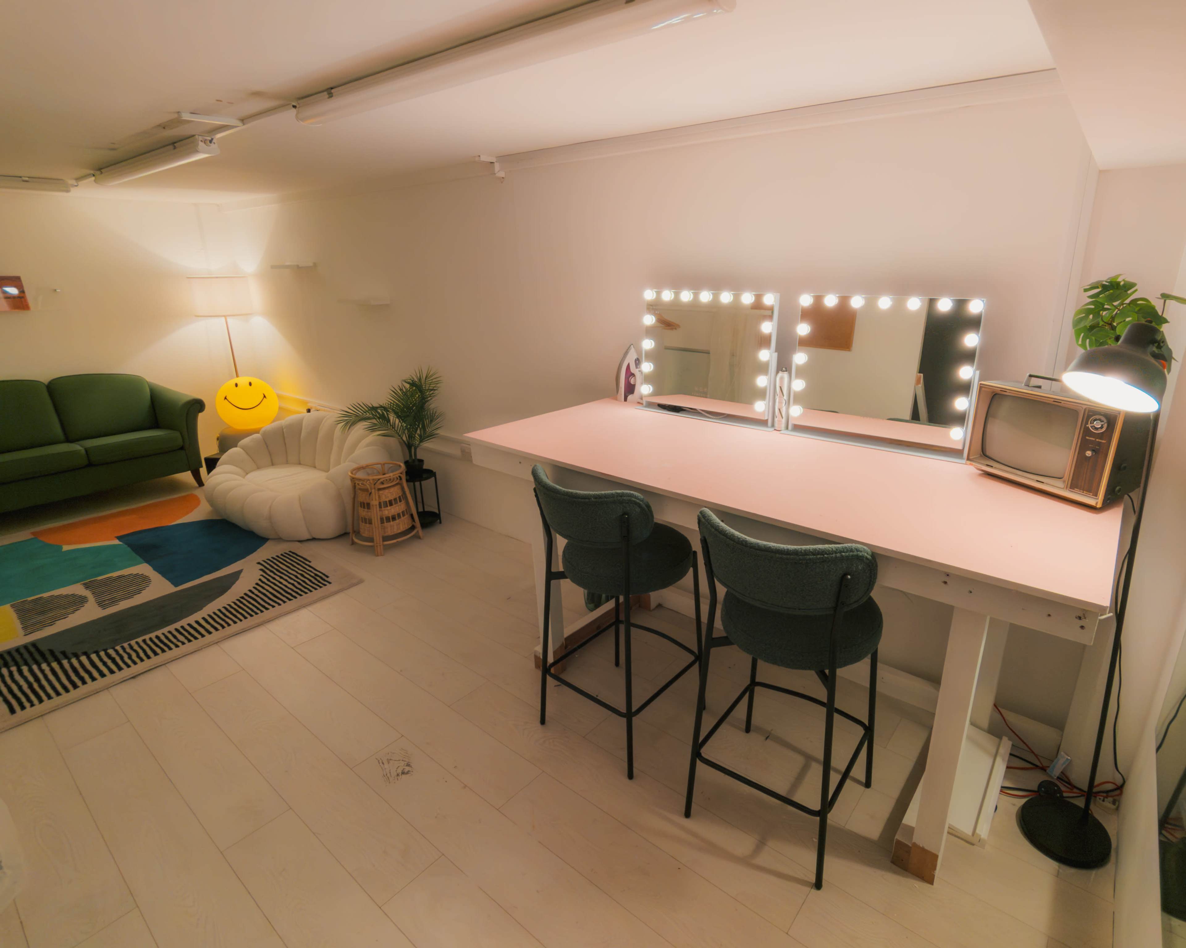 The interior features a cozy room with a green sofa, a warm light source, a large table with illuminated mirrors, and two chairs, accompanied by a vintage television and a white plush seating area on the floor.