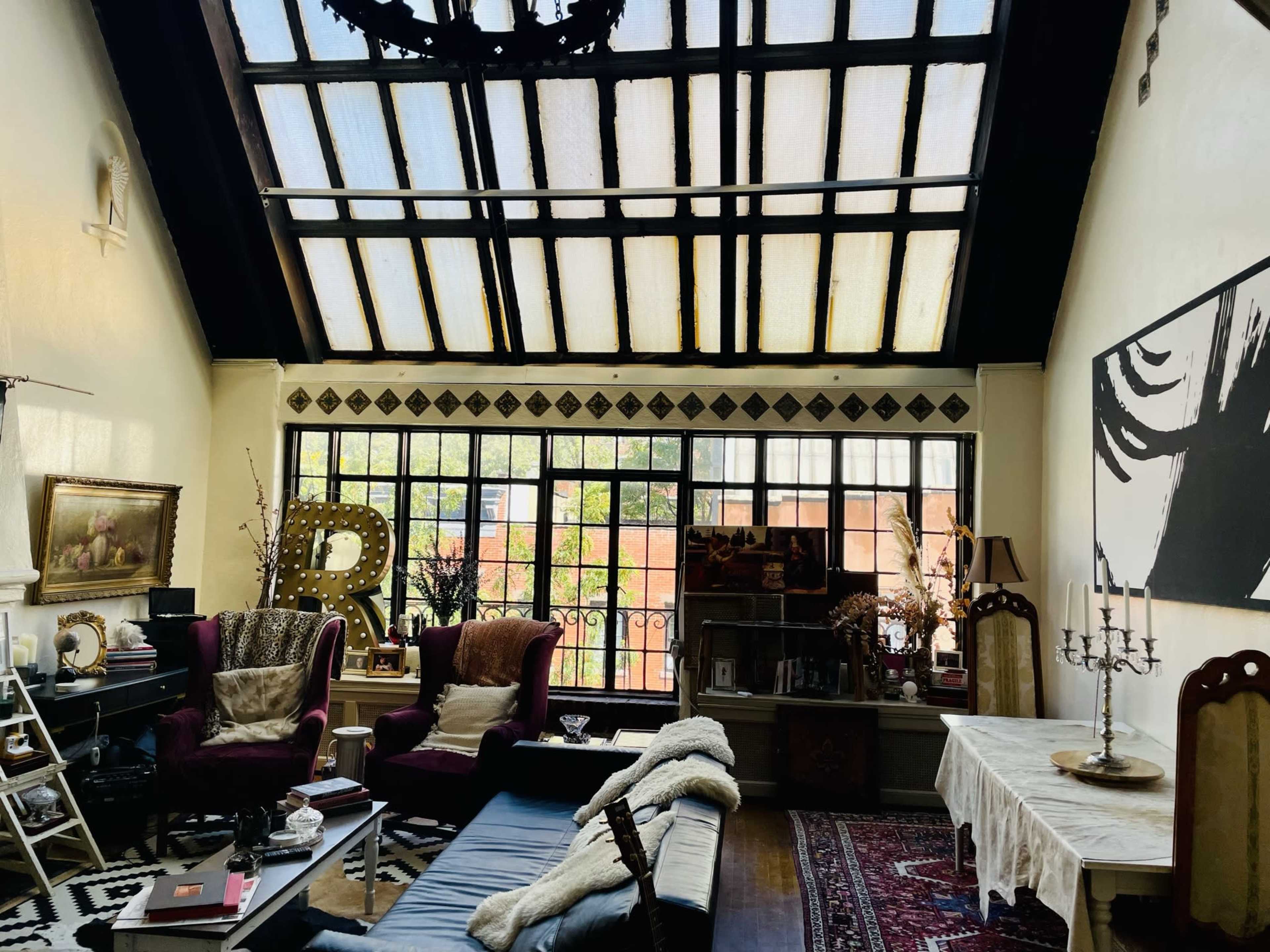 A spacious living room with large windows, a mix of vintage furniture, and decorative elements like a chandelier and artwork.