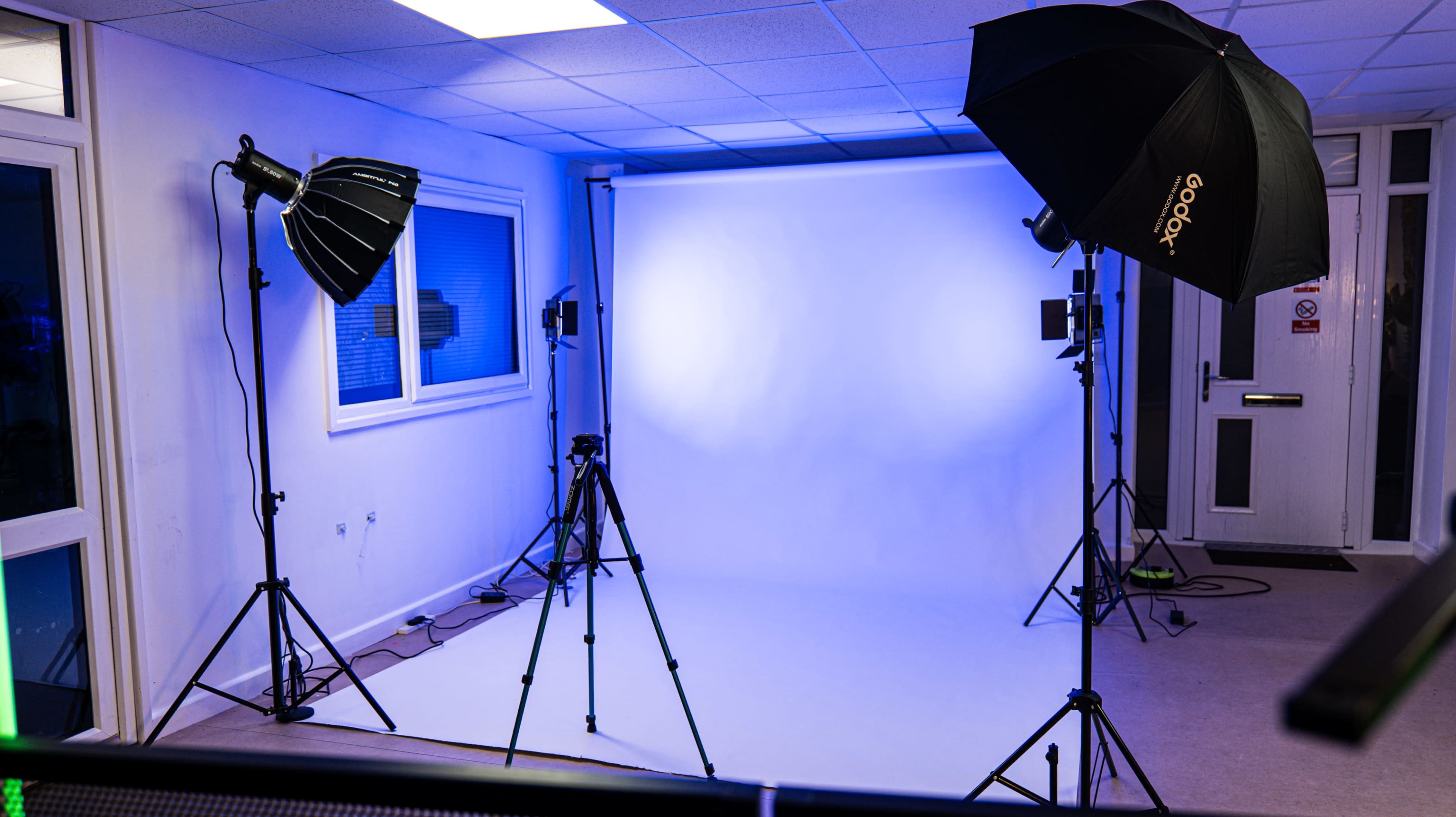The image shows a photography studio with two softbox lights and a backdrop setup for shooting.