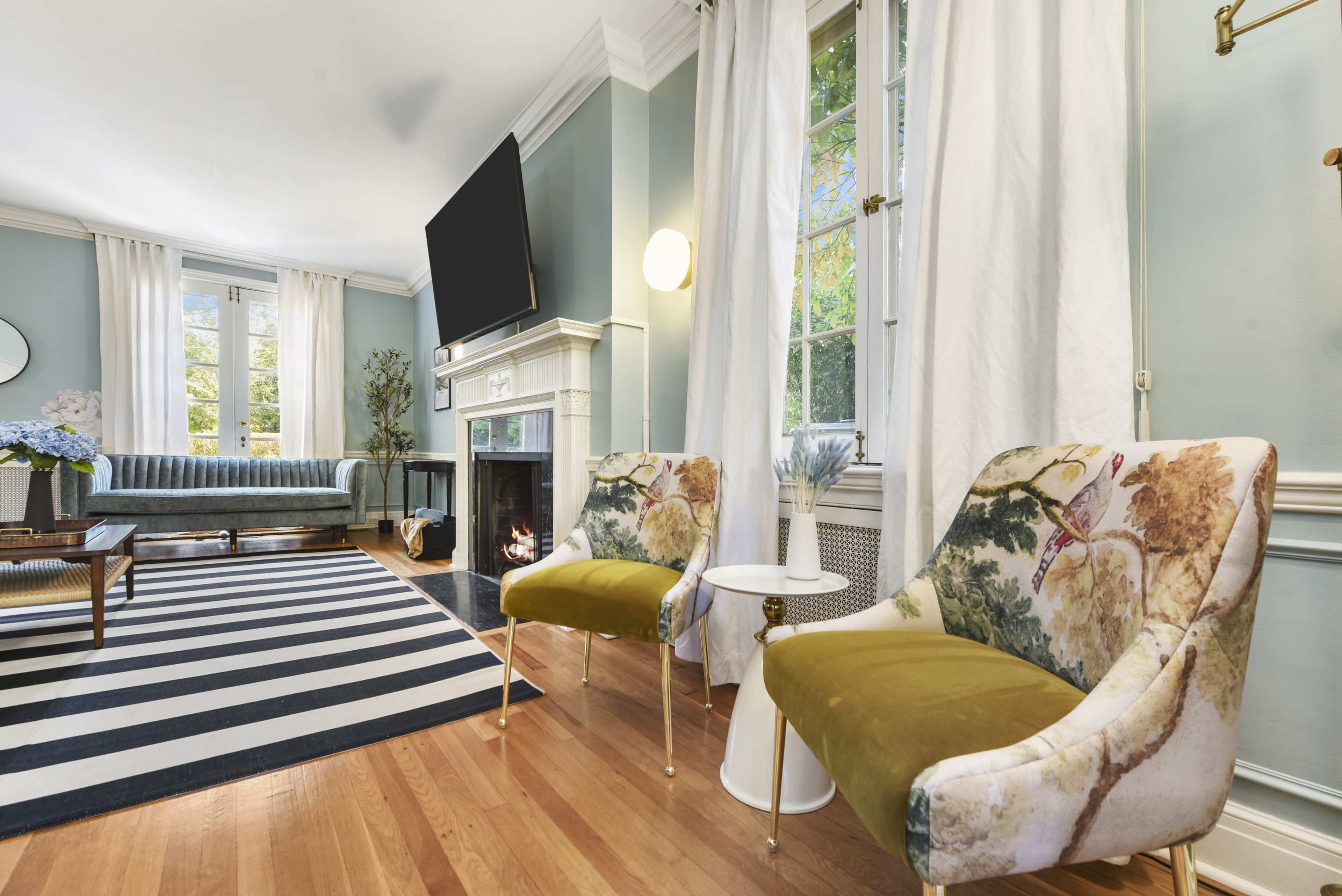 The image shows a stylish living room featuring a striped rug, a fireplace, and two decorative chairs paired with a small side table.