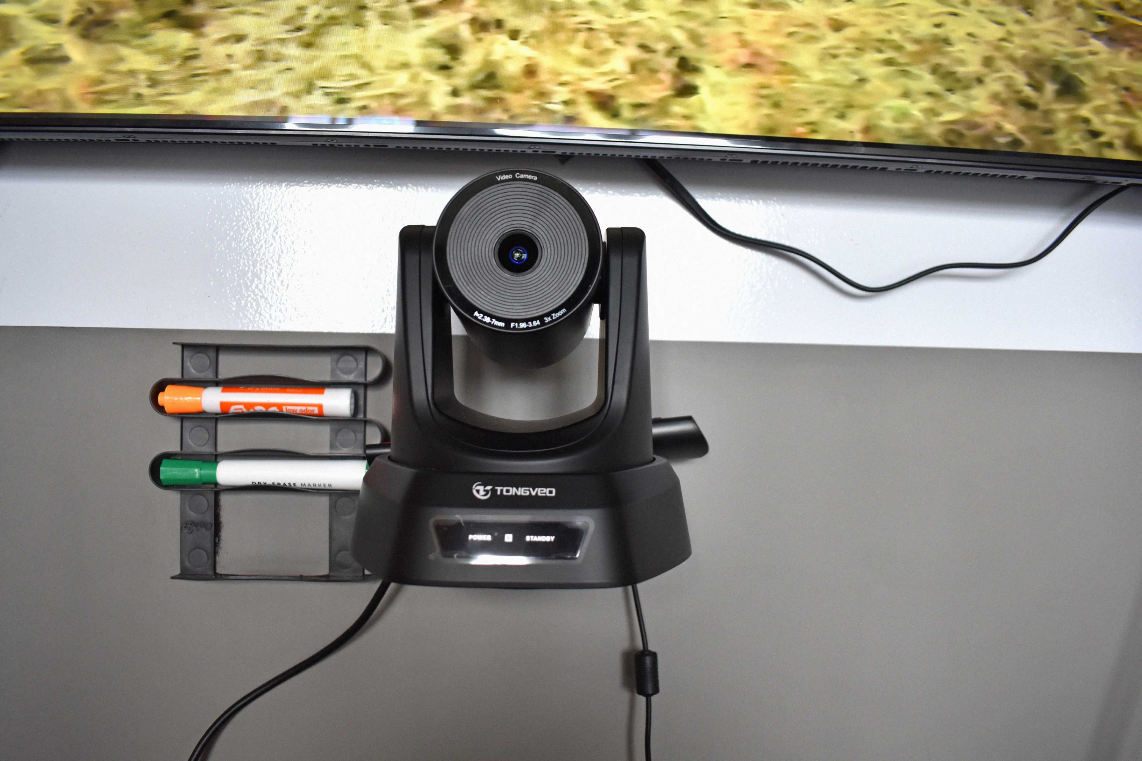A camera mounted on a charging station is placed on a wall alongside markers in a holder.