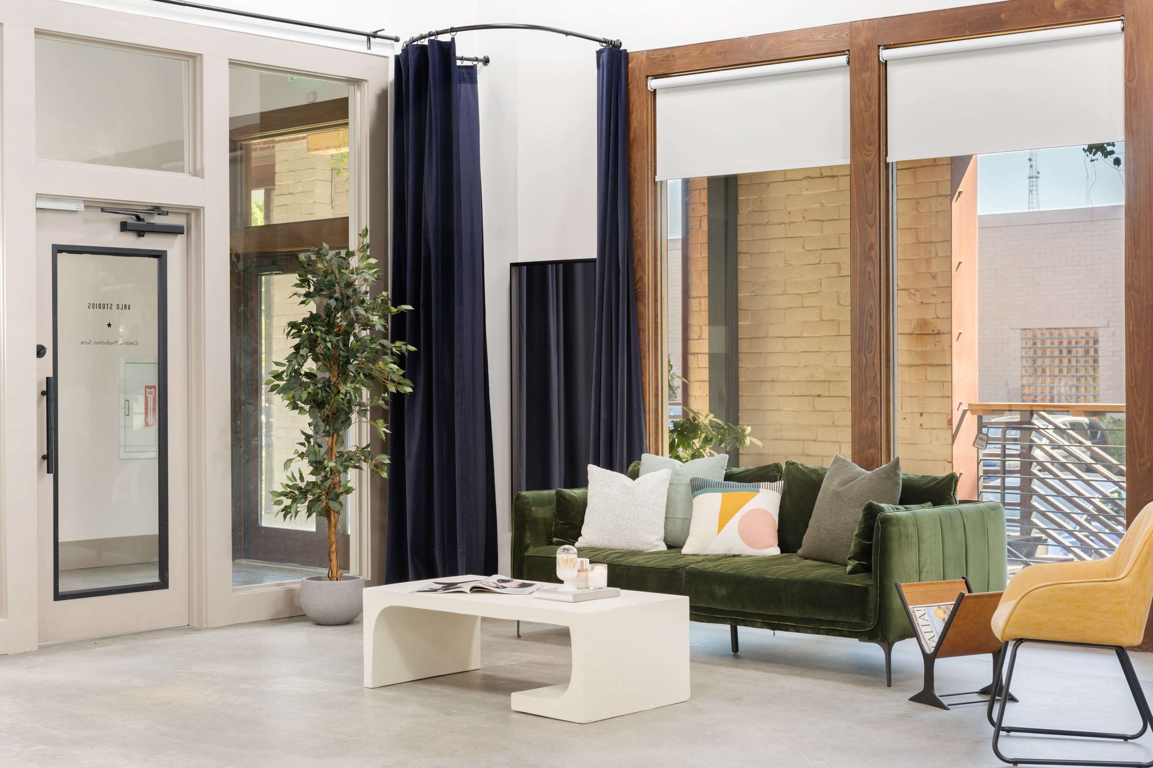 A modern indoor seating area featuring a green sofa, a minimalist coffee table, large windows, and potted plants.